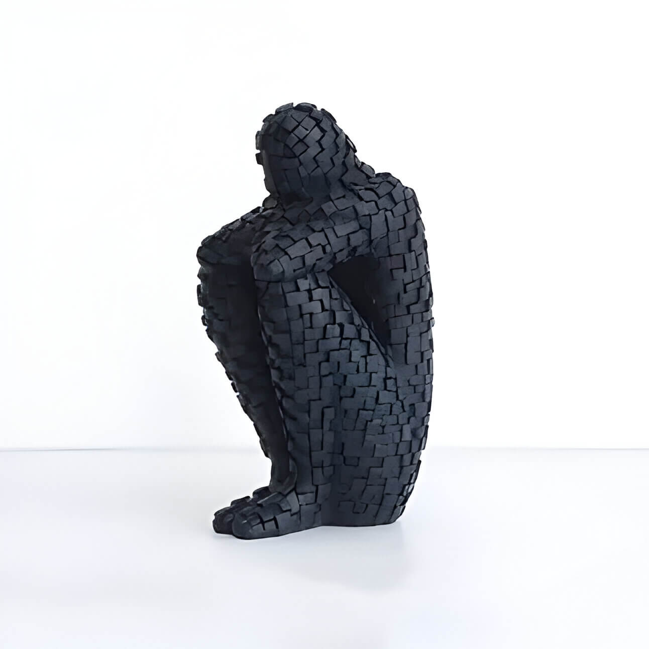 a black textured sculpture of a person sitting with their head resting on their legs