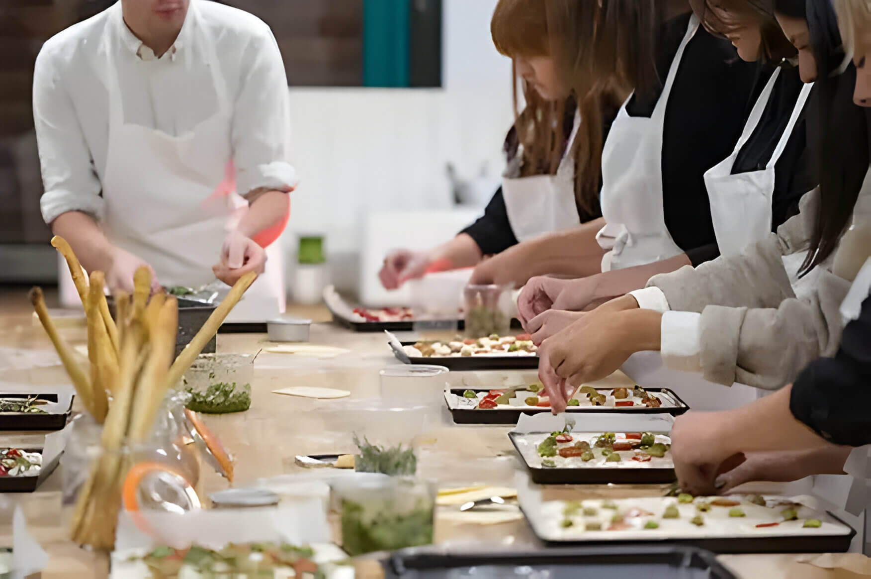 5 students on a cookery course in white aprons with a chef showing them what to do