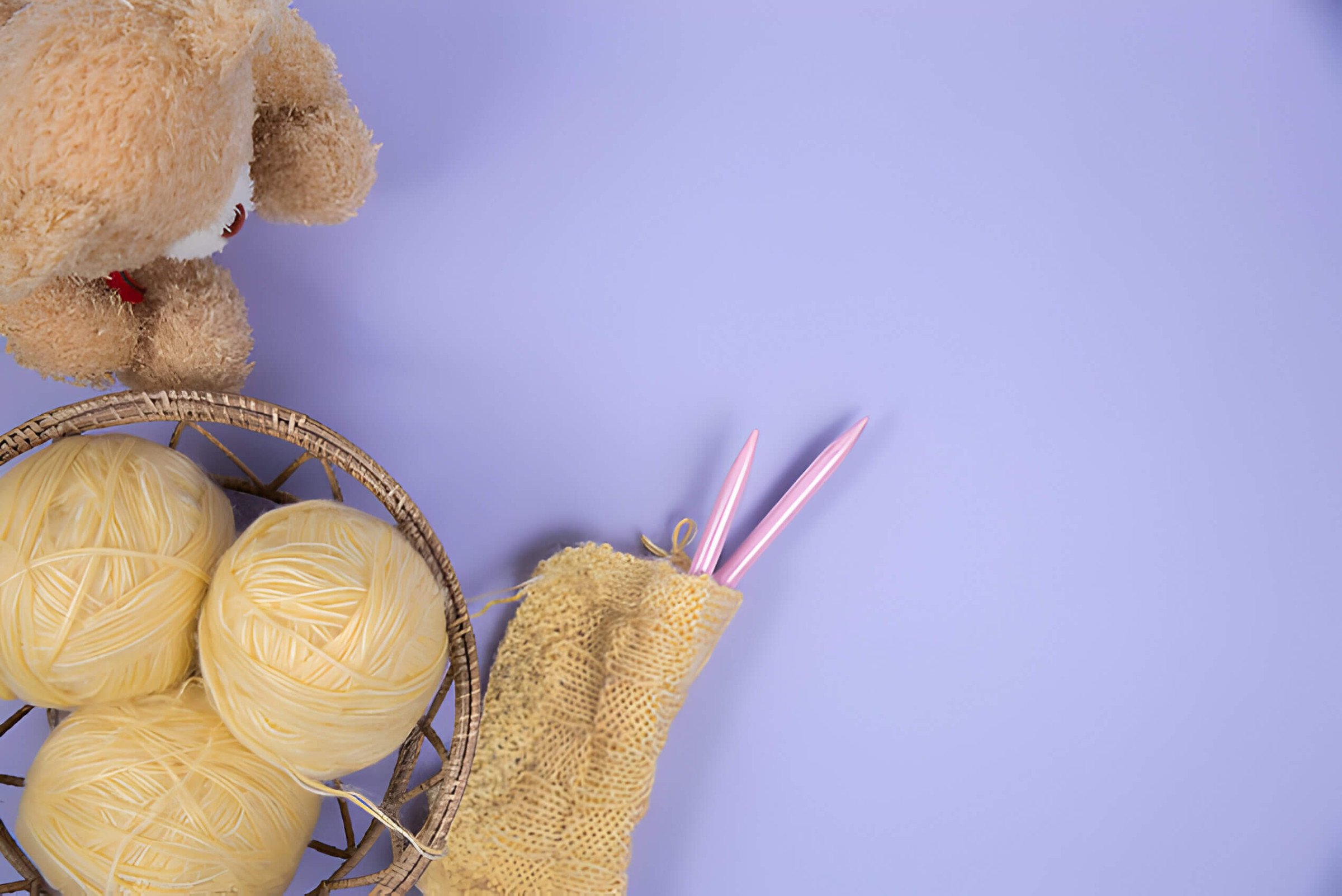 a purple background with yellow yarn and a brown teddy bear