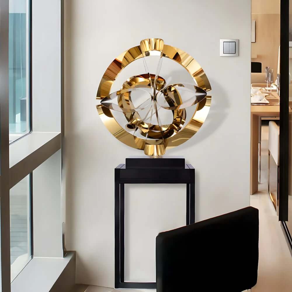 Gold abstract circular sculpture on a black pedestal in a modern interior.