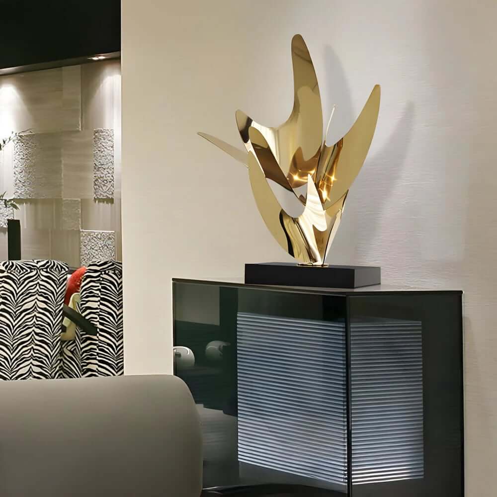 Elegant gold abstract sculpture with smooth, wing-like curves displayed on a black base in a modern living room interior.