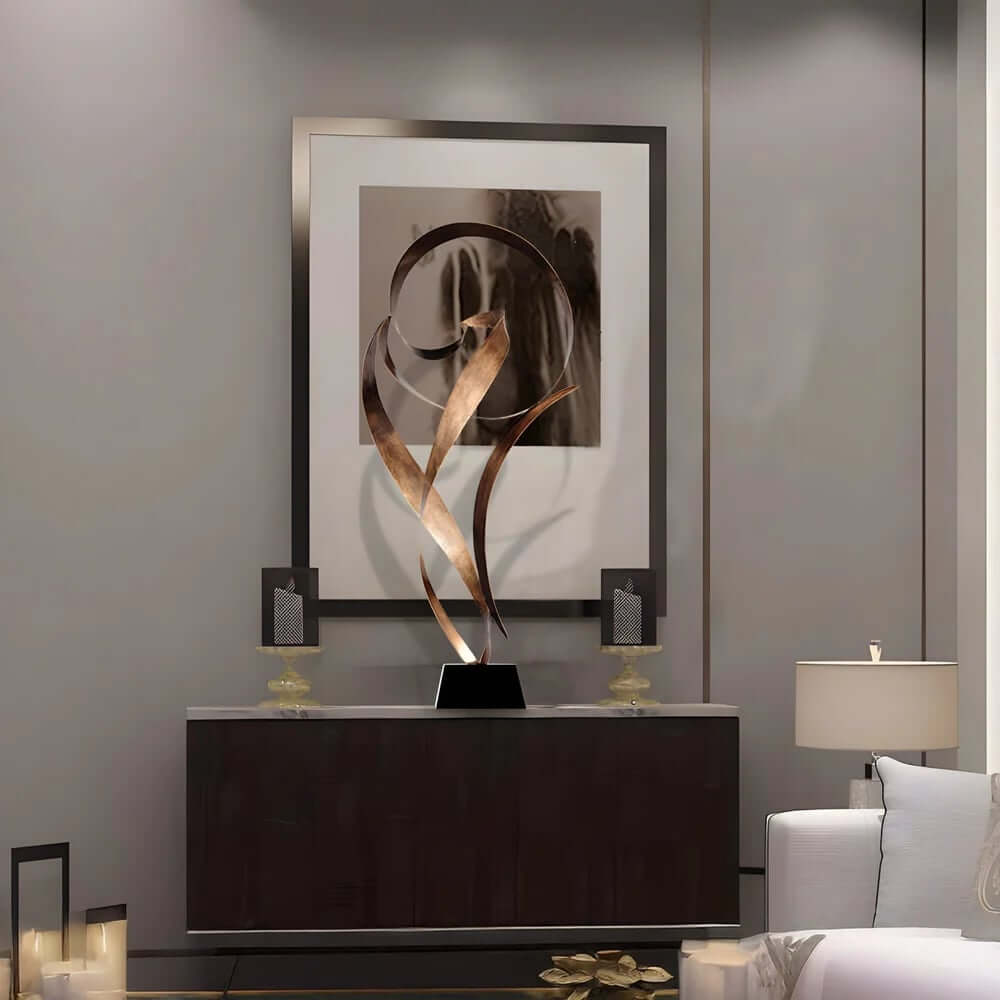 A modern abstract bronze sculpture with flowing curved shapes displayed on a black base atop a console table in an elegant living room with minimalist décor and soft lighting.