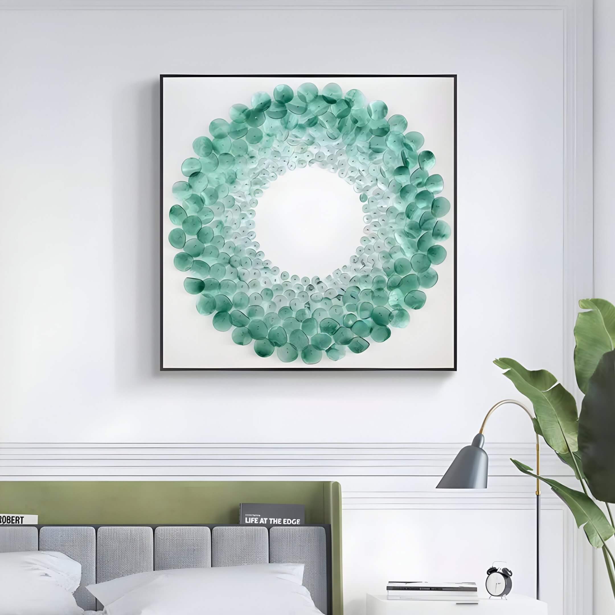 Green circular acrylic wall art with layered translucent discs arranged in a wreath-like design, displayed above a modern bed in a minimalist bedroom.