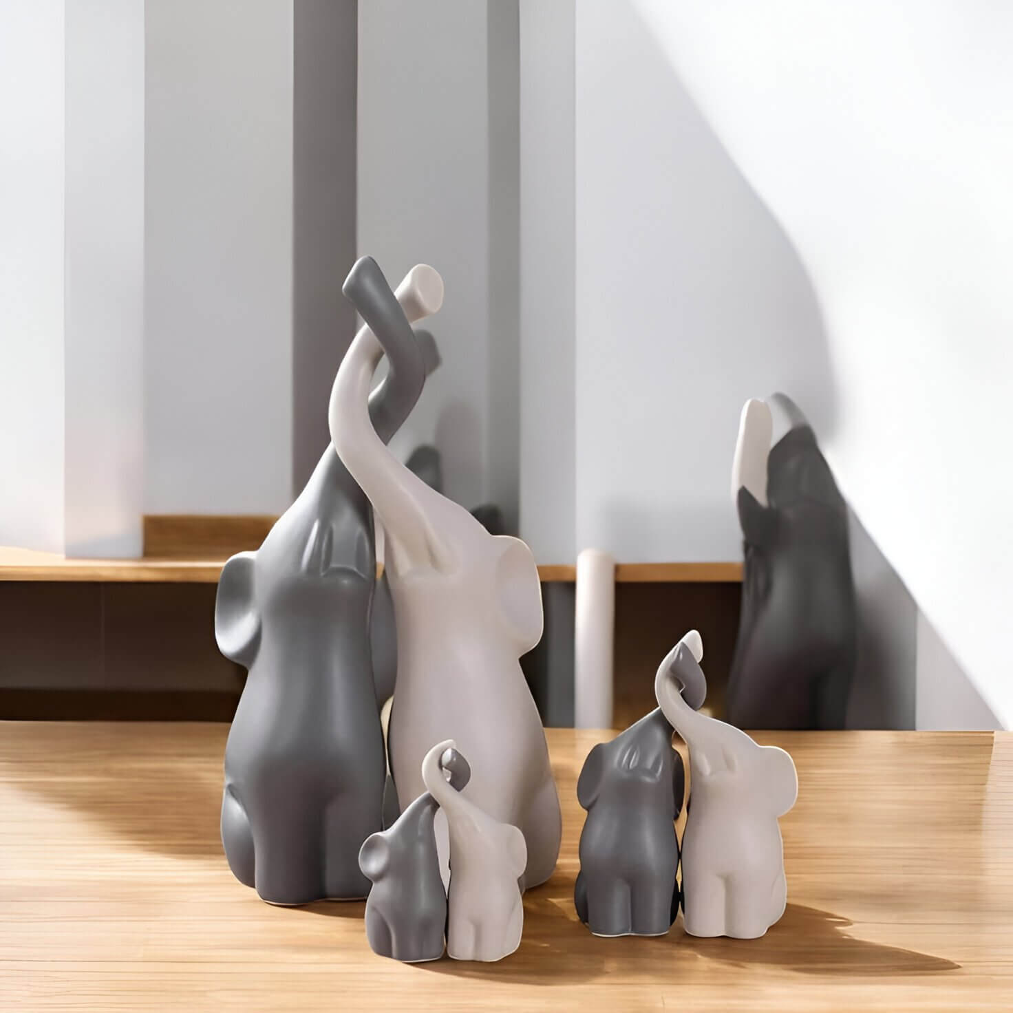 Charming minimalist elephant sculptures in grey and white, displayed in varying sizes on a wooden surface, symbolising family unity and love in a modern decor setting.