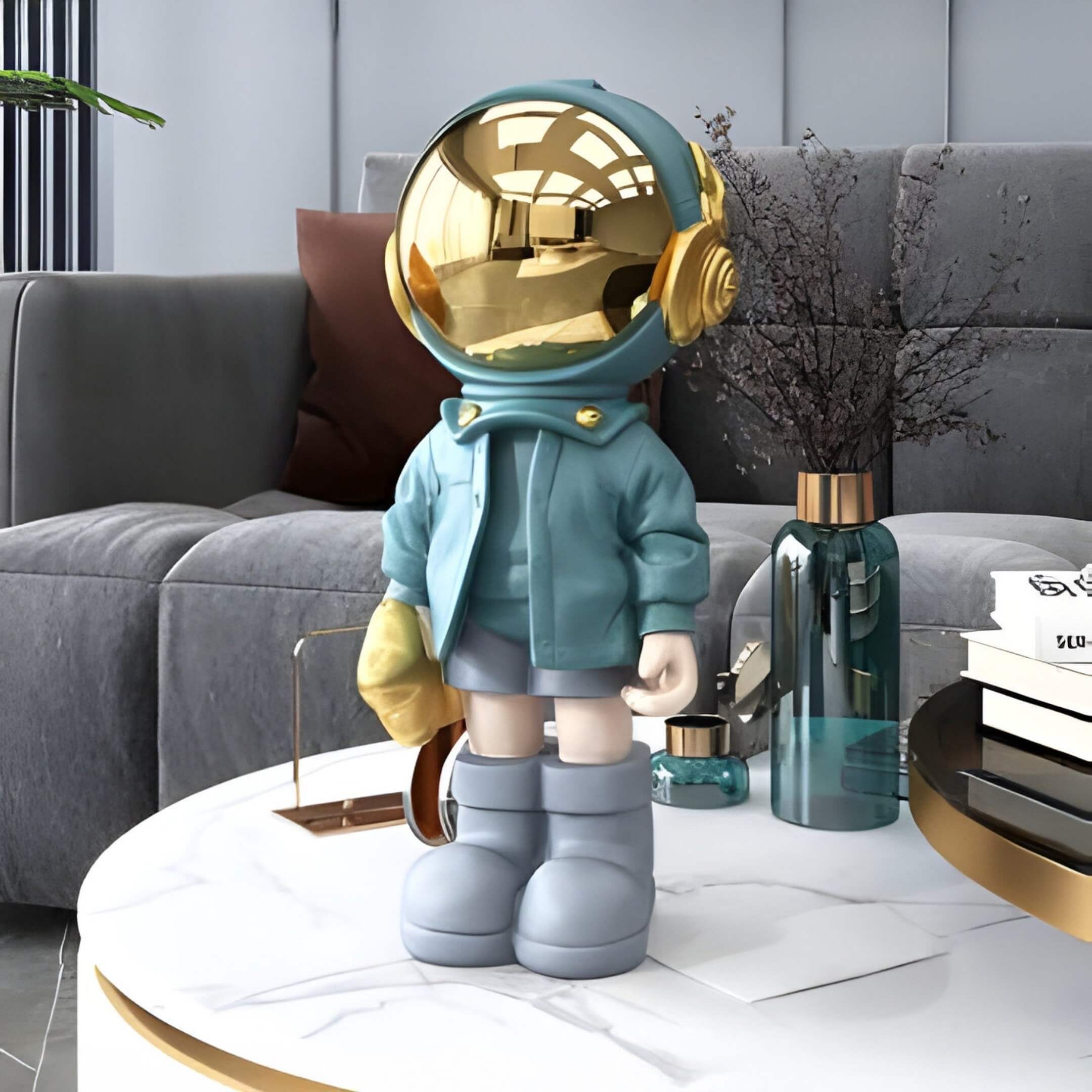 A Galactic Blue Astronaut Sculptures by Giant Sculptures, featuring a gold helmet and teal jacket with gray boots, stands on a white marble table. A modern gray sofa, decorative plants, and a teal vase create the background.