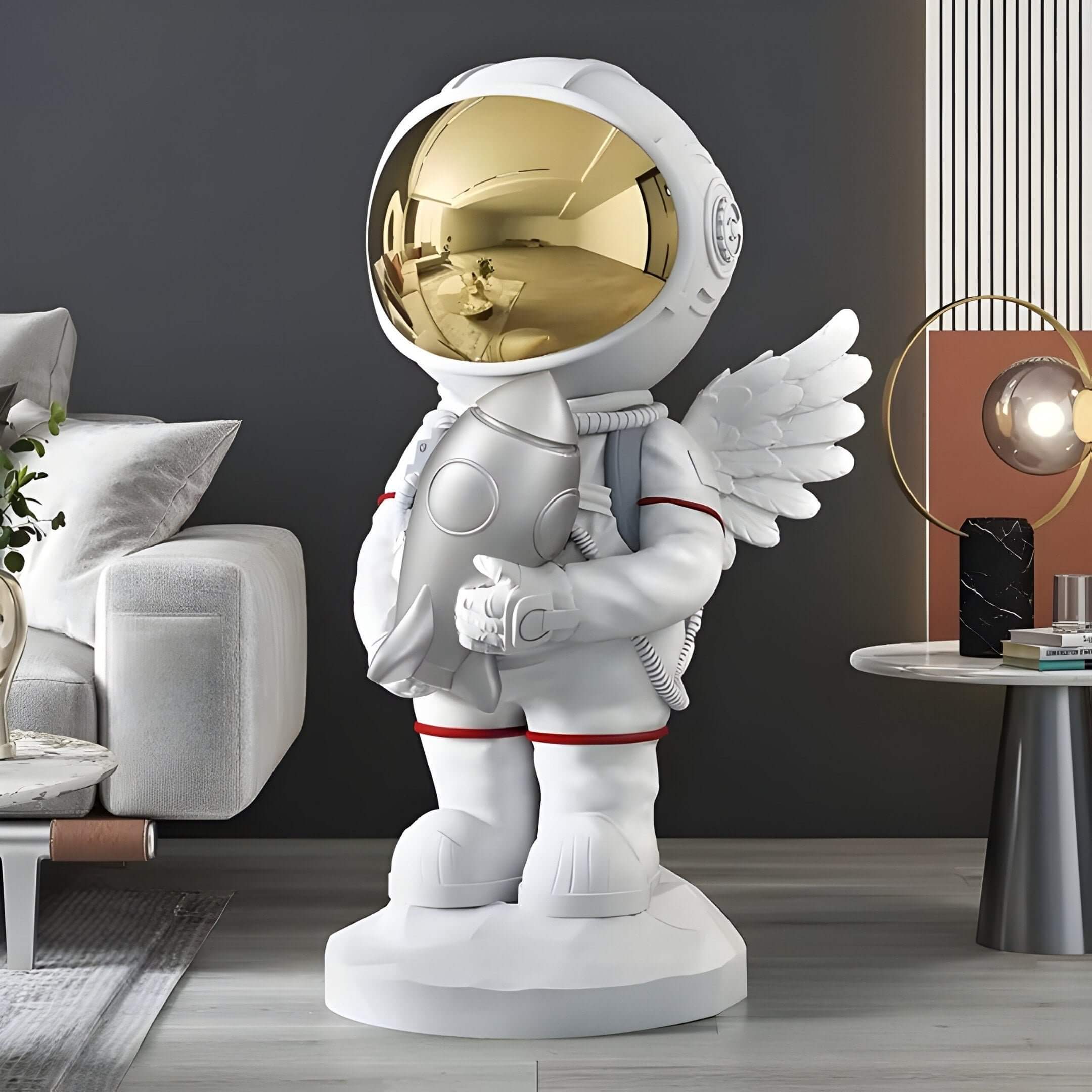 White astronaut sculpture with a gold visor and wings holding a rocket, standing on a pedestal in a modern living room next to a sofa and side table.