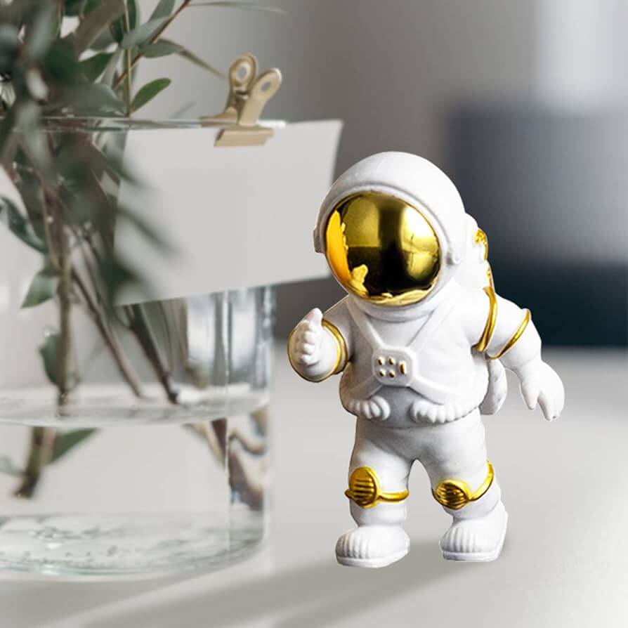 Small white astronaut figurine with golden visor and details standing on a table beside a glass vase.