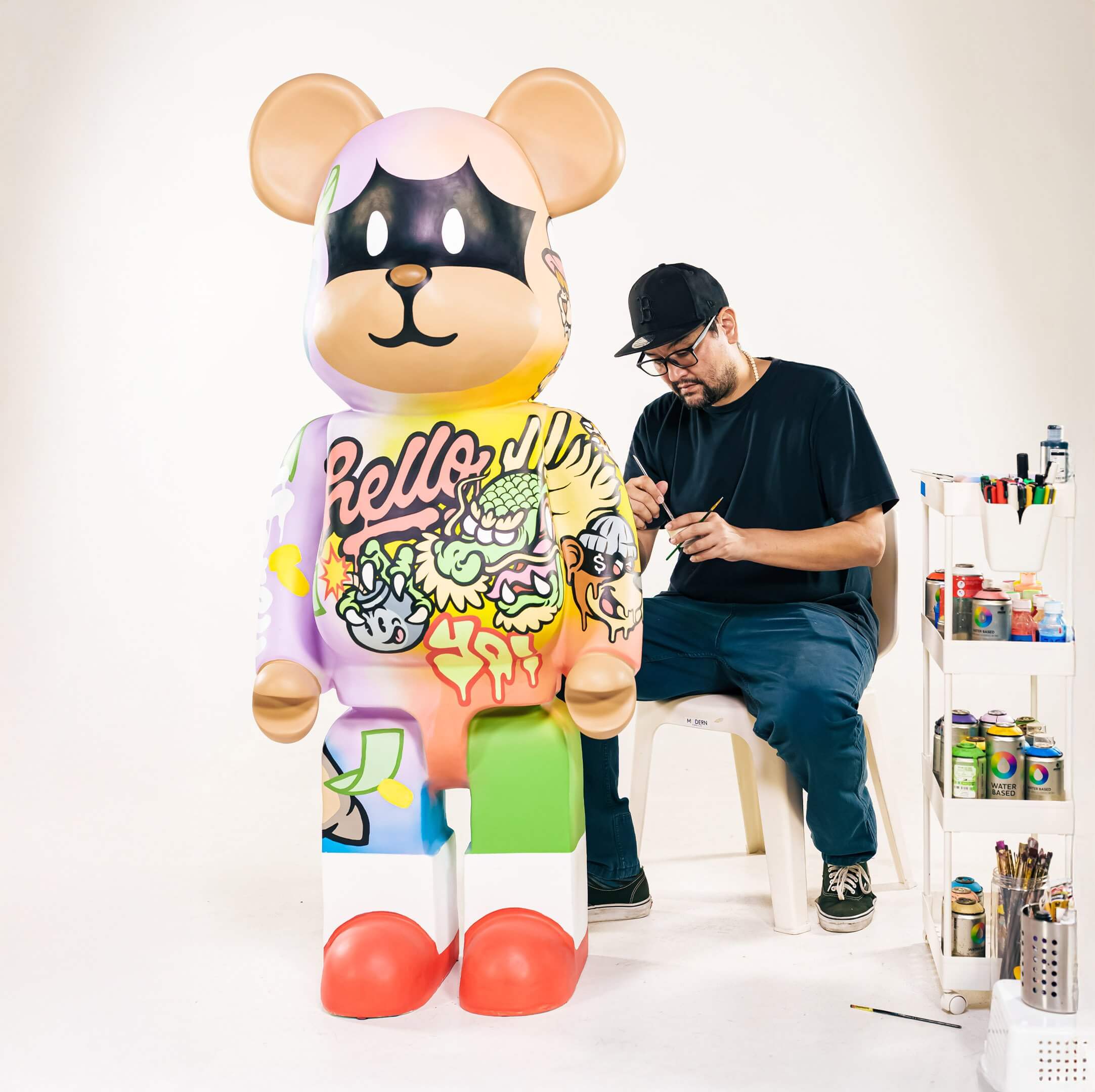 Artist hand-painting the Lucky Paws Bear Sculpture, a large bear-shaped figure featuring bold street art graphics, cartoon motifs, and vibrant colors in a studio setting