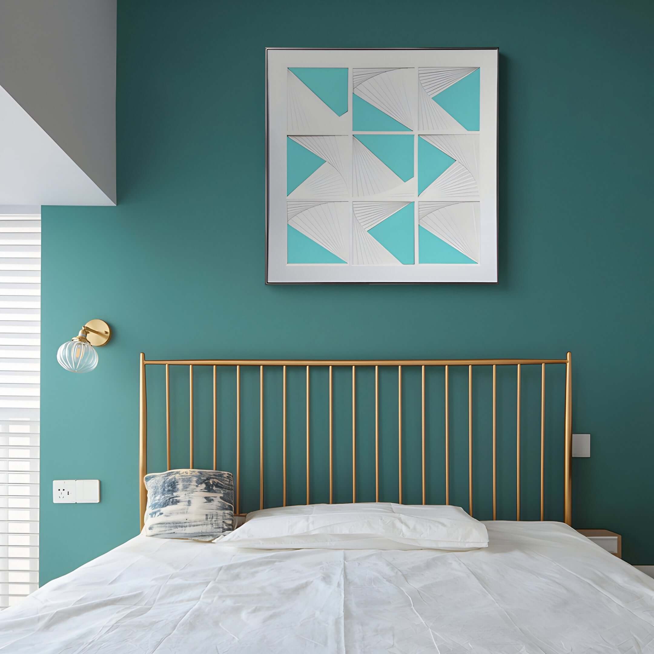A modern bedroom with a teal accent wall showcases a gold metal headboard and white and gray pillows. Above, the Prismatics Turquoise Geometric Cardboard Carving Wall Art by Giant Sculptures adds flair. A round wall lamp with a clear globe shade completes this contemporary interior.