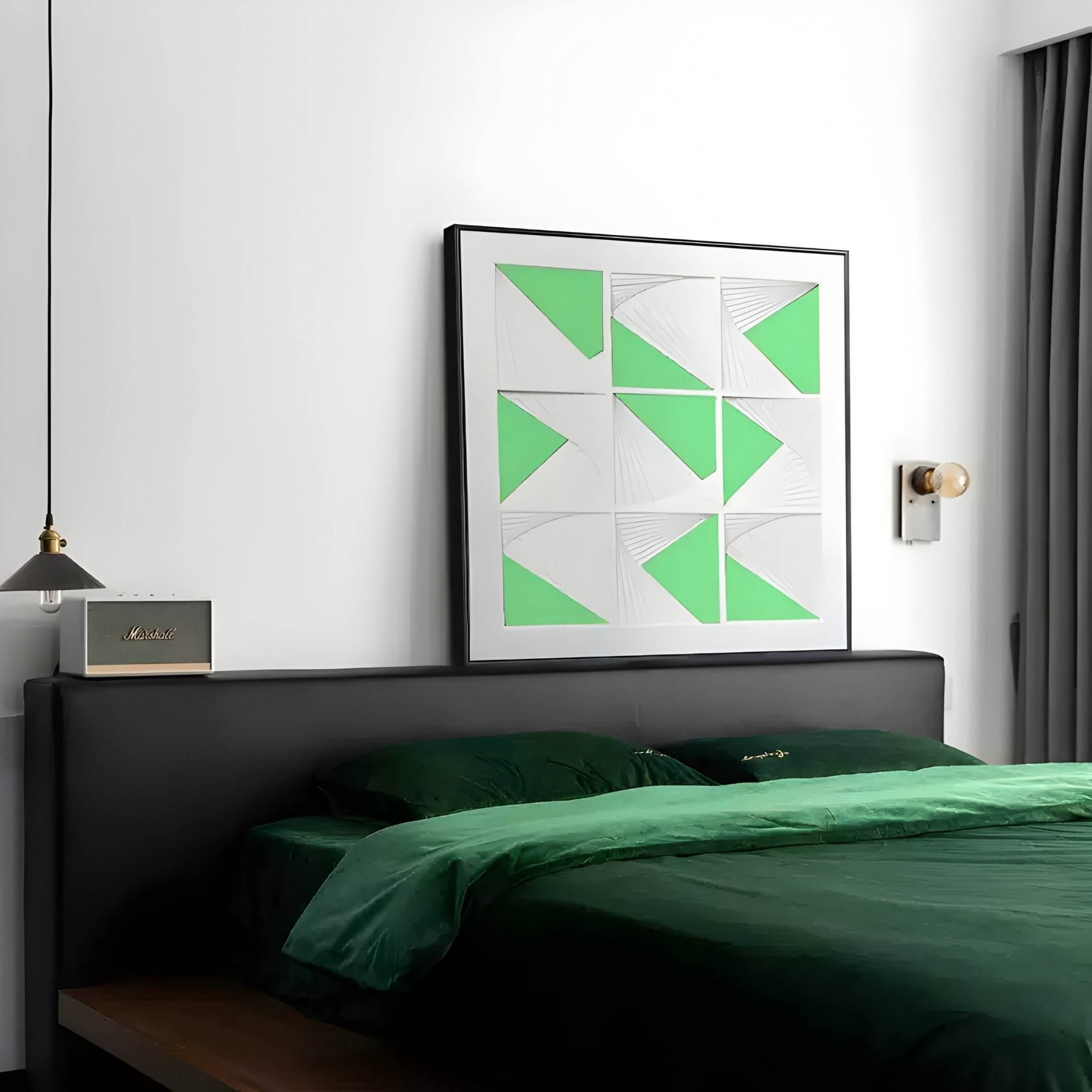 A modern bedroom showcases a dark green bedspread and pillows. Above the bed, the captivating Prismatics Green Geometric Cardboard Carving Wall Art by Giant Sculptures adds charm. A small pendant light, a bedside lamp, and a gray curtain partially covering the window enhance the ambiance.