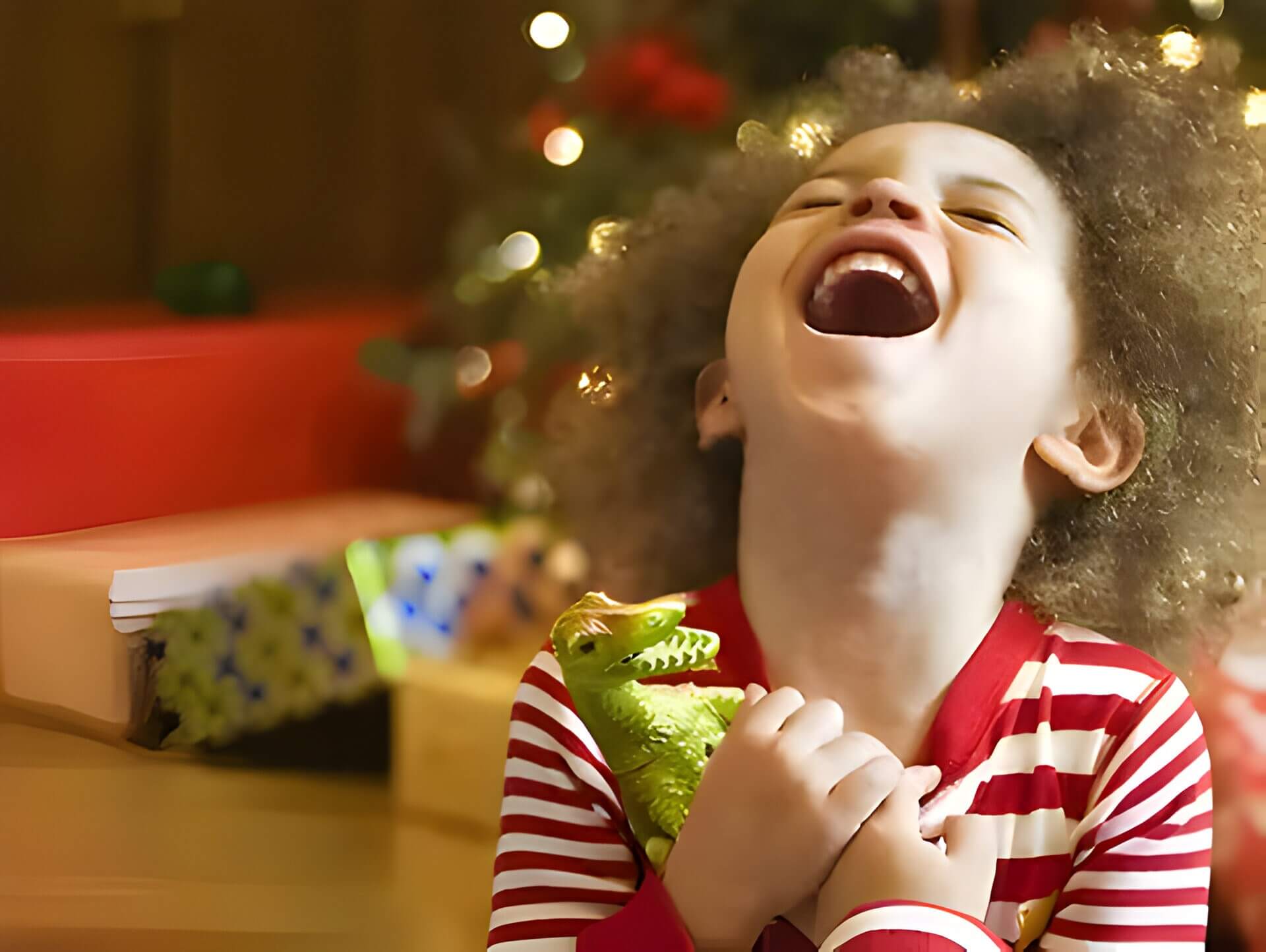a young boy cuddling a dinosaur in front of a Christmas tree