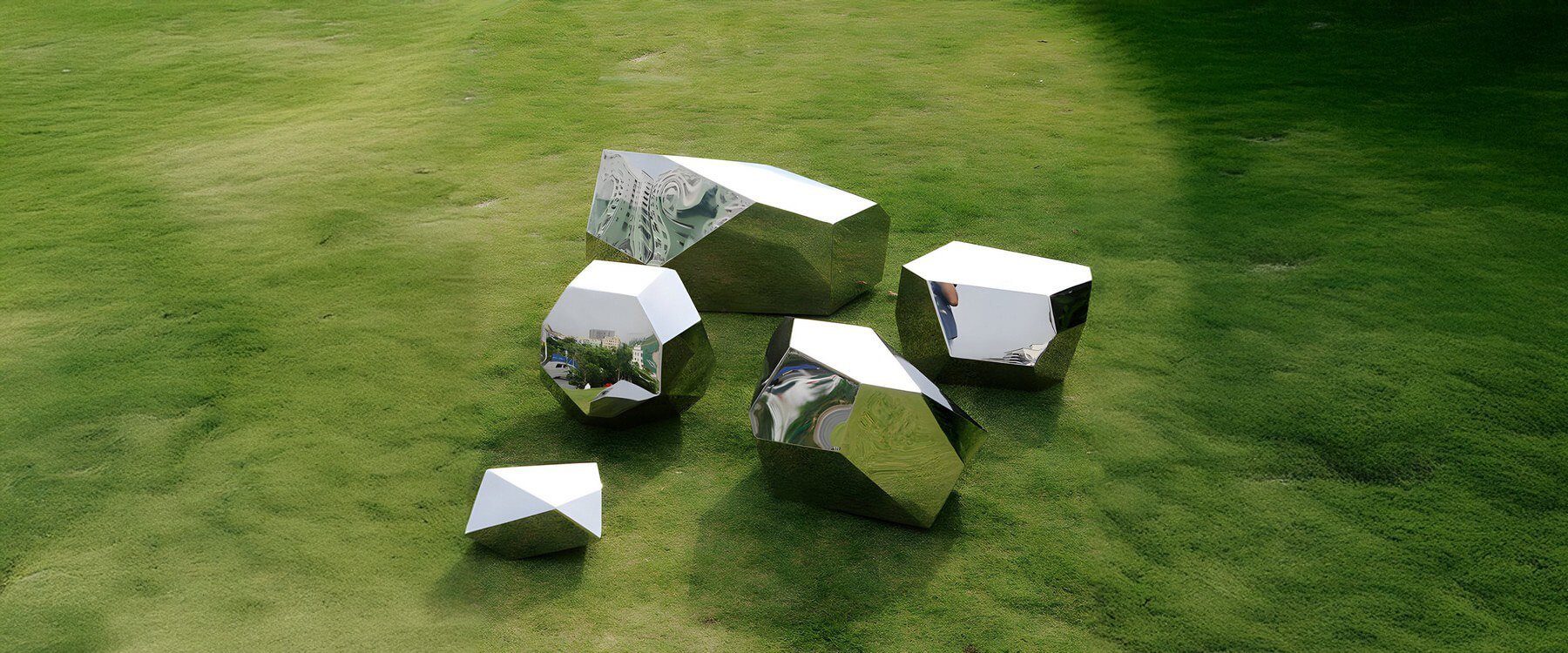 Cluster of geometric mirrored sculptures arranged on a lush green lawn, reflecting the natural surroundings and open sky.