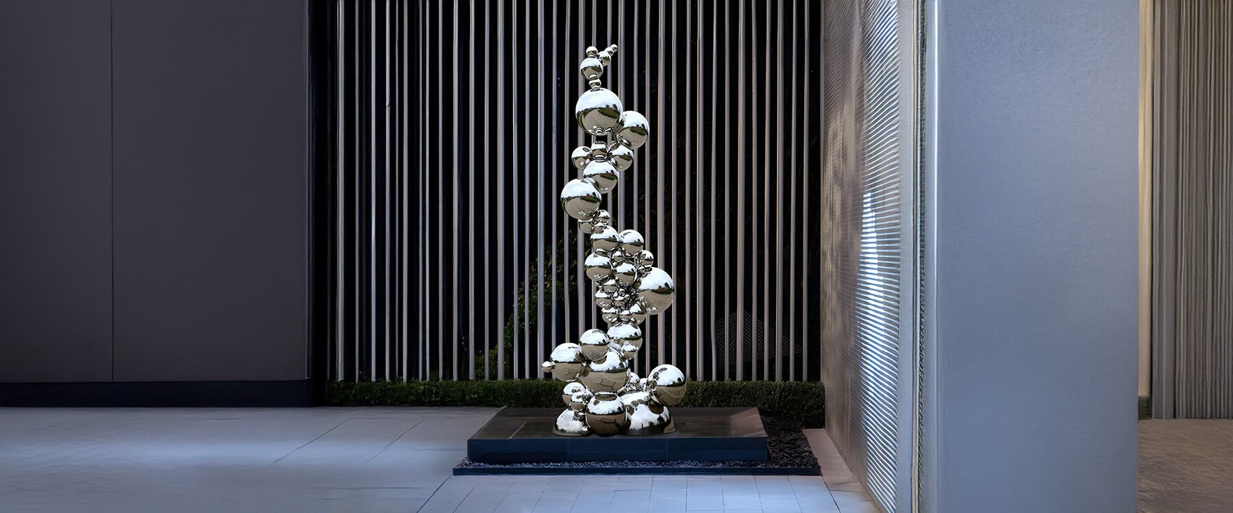 A modern outdoor sculpture featuring stacked metallic mushroom-like forms, set on a black platform against a striped wall.