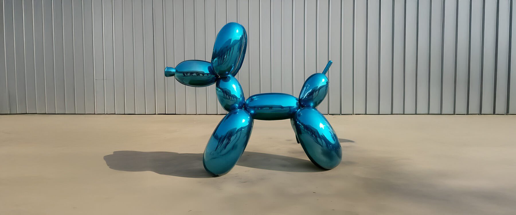 Vibrant blue metallic balloon dog sculpture displayed outdoors on a neutral surface, set against a corrugated metal backdrop.