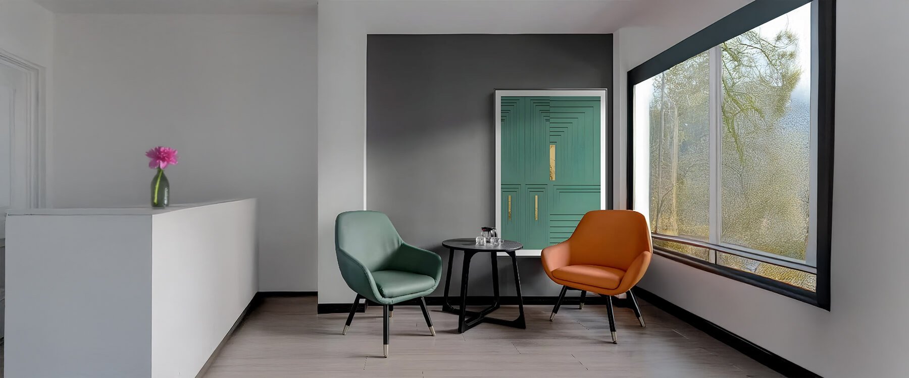 A contemporary office lounge with a minimalist reception desk, two stylish chairs in green and orange, and a round coffee table near a large window.