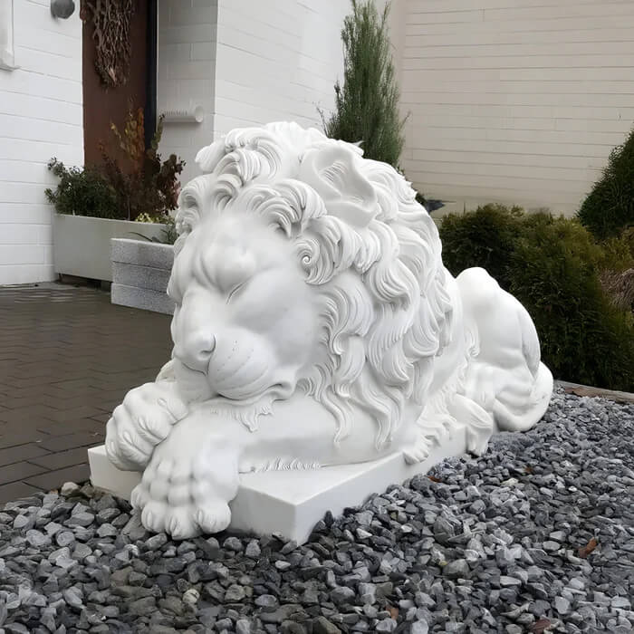 A detailed, intricately carved lion sculpture lying on a stone base, surrounded by landscaped greenery.
