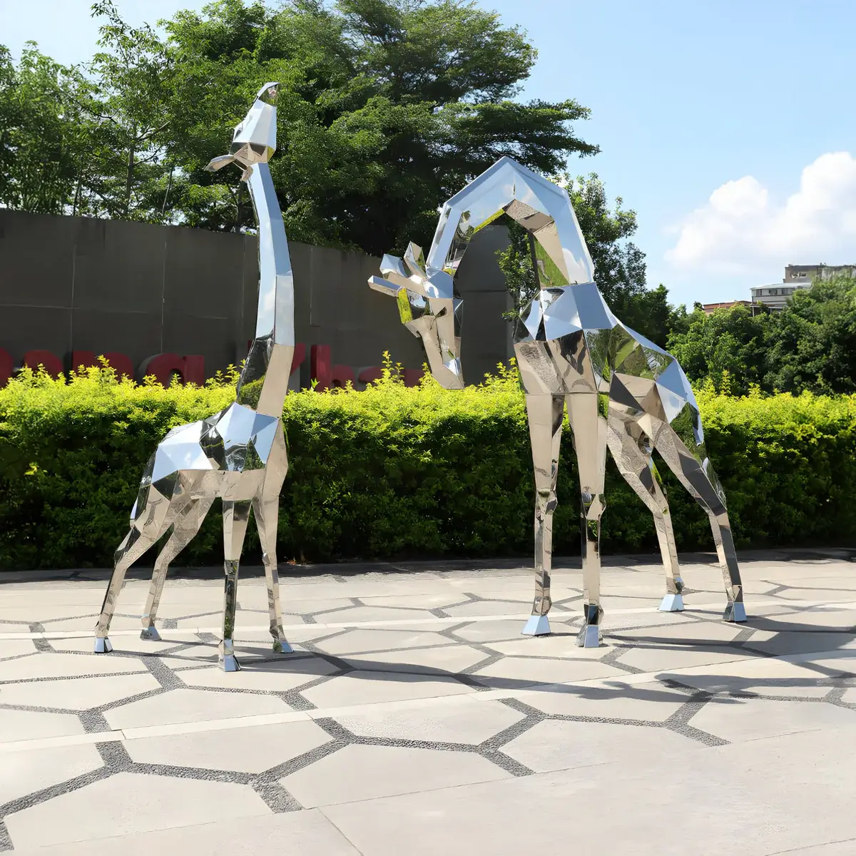  A pair of abstract geometric giraffe sculptures made of polished metal, standing in an open landscaped area.