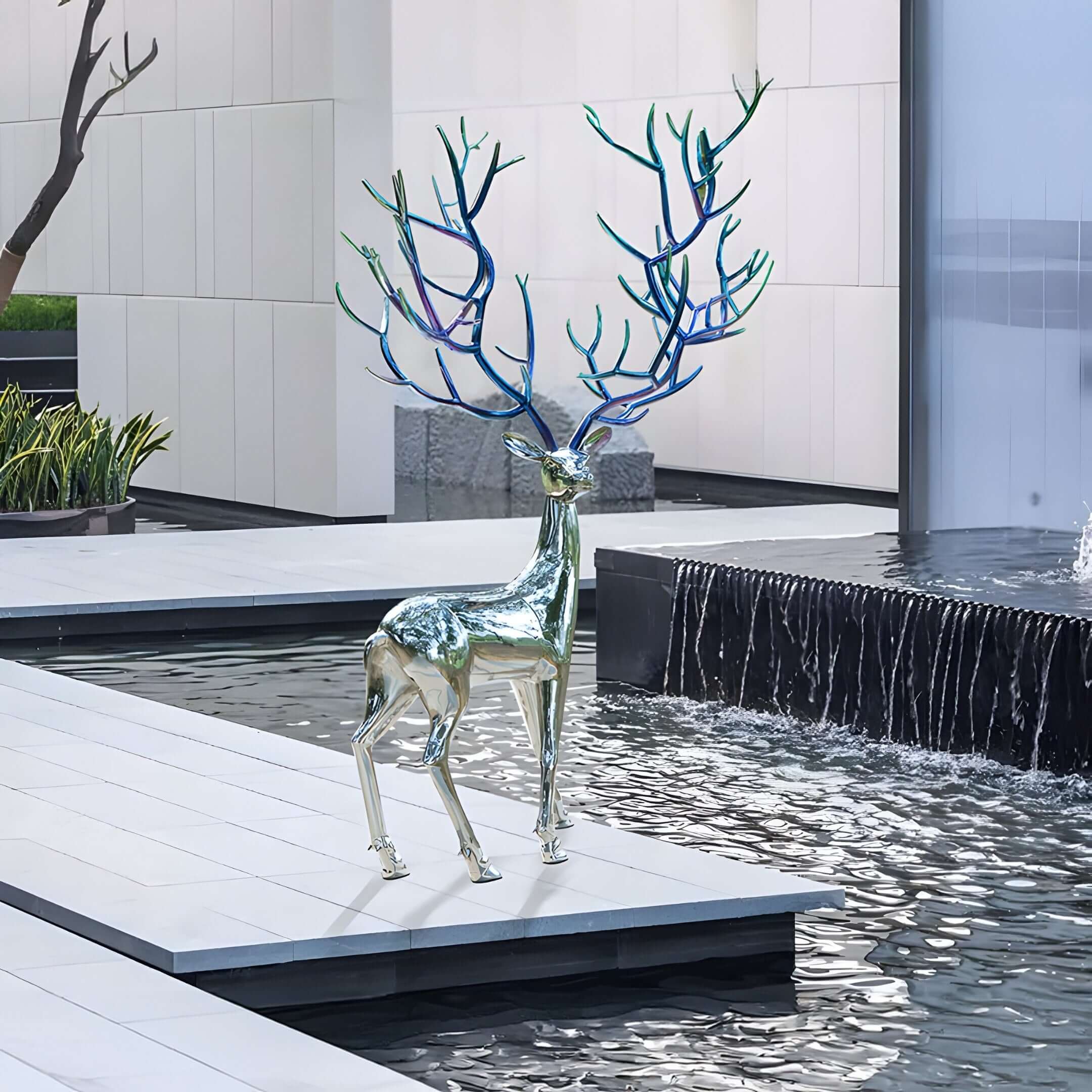 Chrome Deer Sculpture by Water – A metallic deer statue with artistic blue antlers, placed beside a reflecting pool in a modern space.