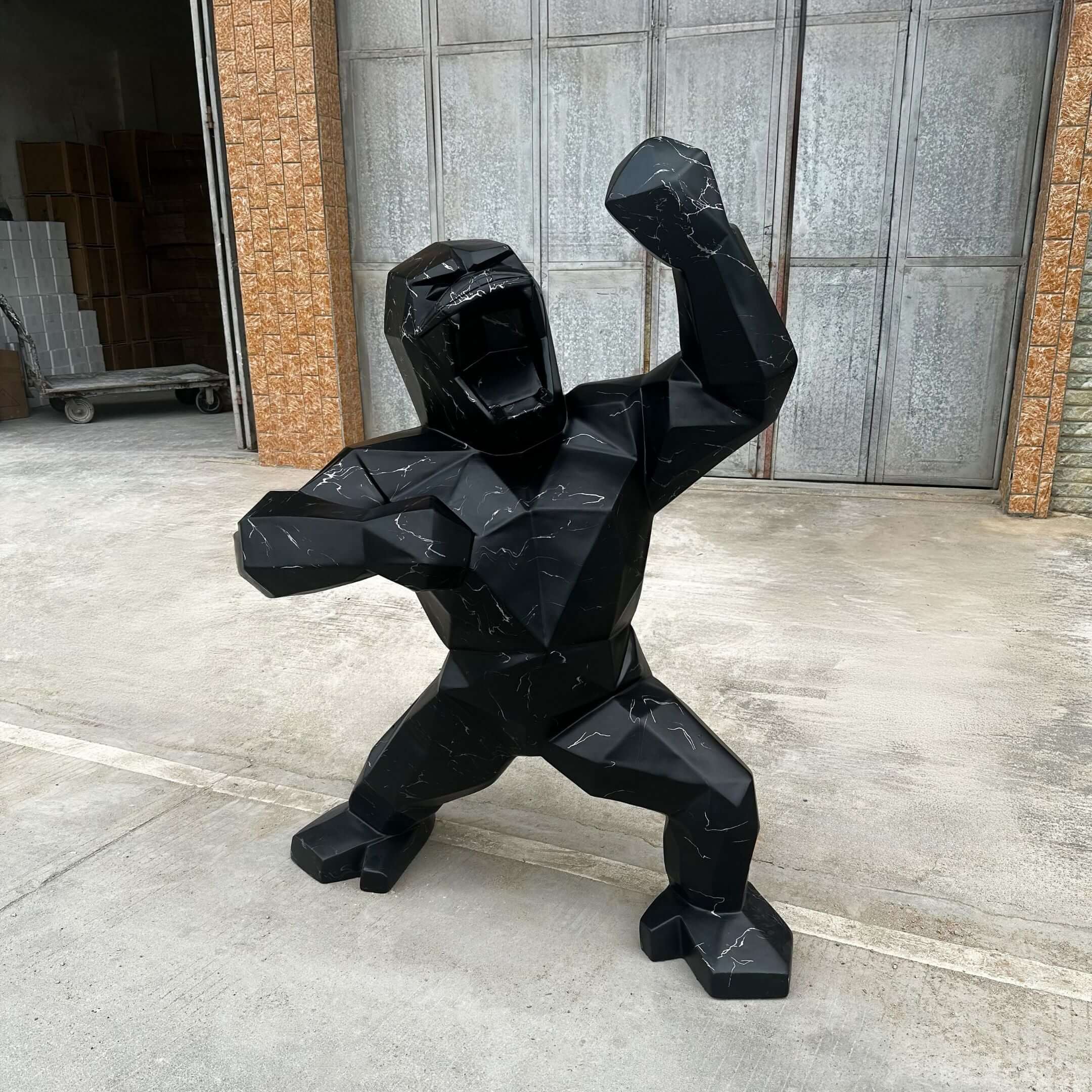 Striking black geometric gorilla sculpture with white marble veins, posed dynamically in an outdoor industrial setting with metal and brick textures in the background.