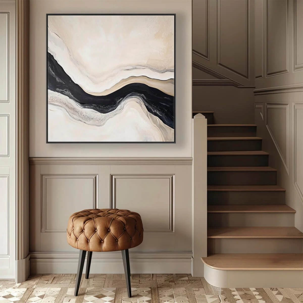Square abstract painting with a wavy black band through beige and cream layers, hanging above a tufted leather stool in a neutral stair hall with paneled walls and wooden steps.