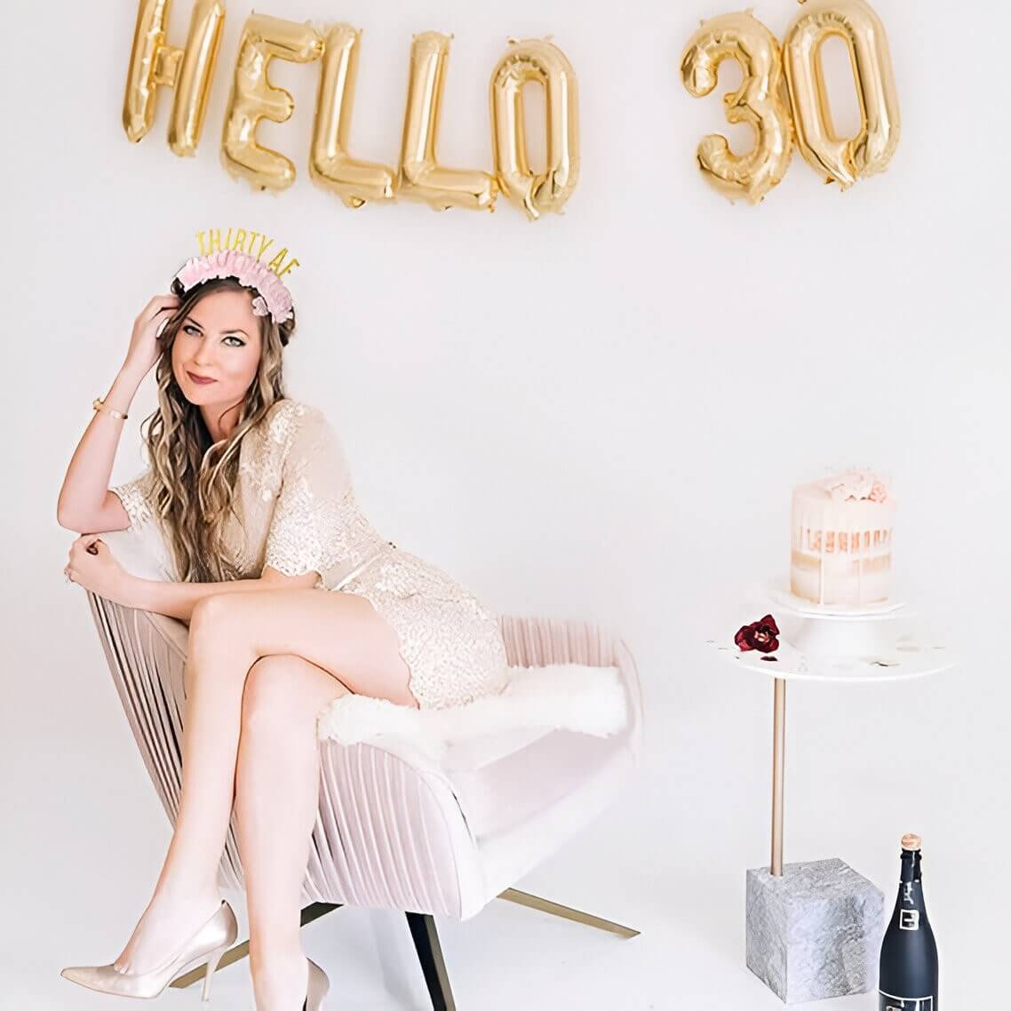 a woman sitting in a cream chair with a cake and 30 years balloons