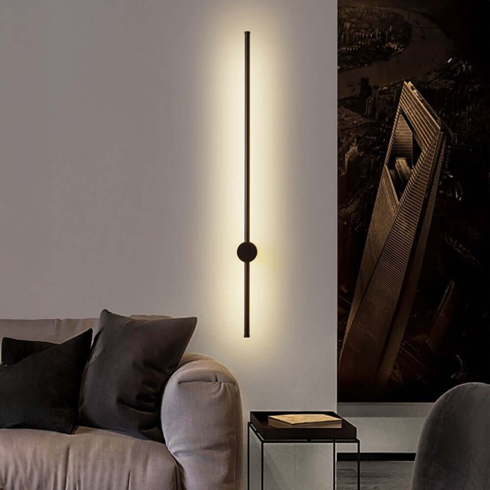 Nordic stick wall light casting a warm vertical glow behind a minimalist black rod fixture, mounted beside a modern sofa in a contemporary living room setting