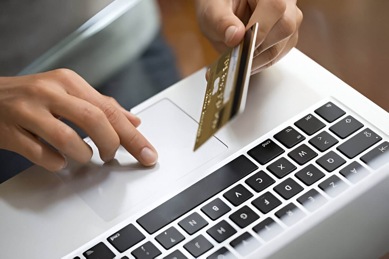 Close-up of a person using a laptop and holding a credit card, illustrating online shopping or digital payment processing.
