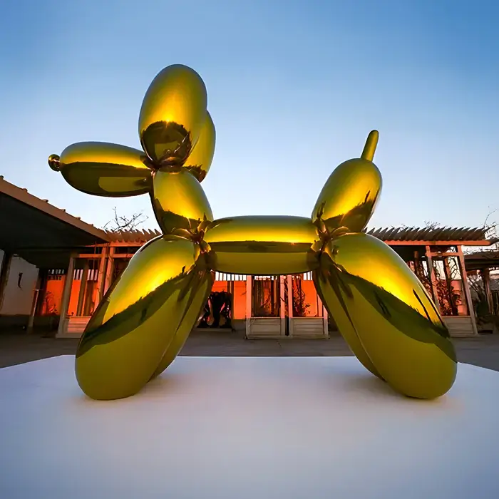 A large, polished gold balloon dog sculpture resembling a playful, inflated design, positioned outdoors.