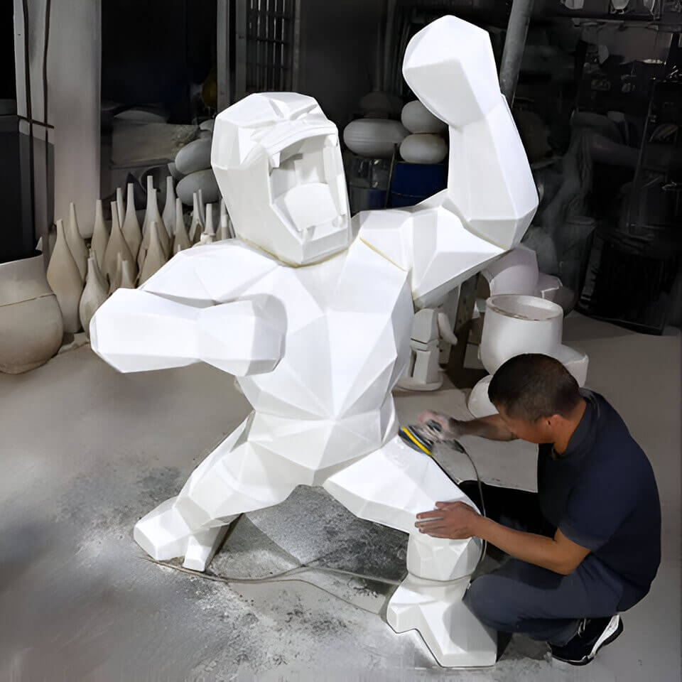 Artisan refining a white resin gorilla sculpture with a sanding tool, showcasing craftsmanship in creating detailed and modern sculptures.