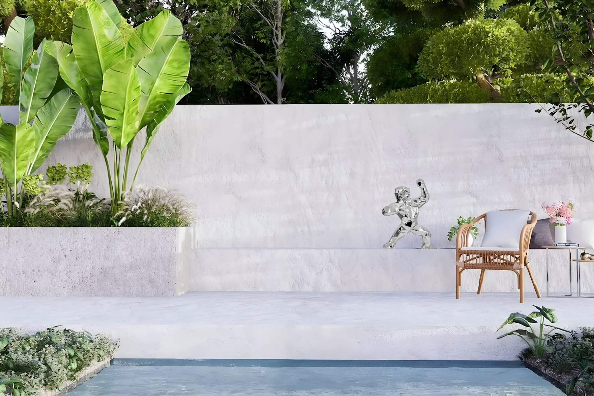 Chrome gorilla garden sculpture displayed on a modern white terrace, surrounded by lush greenery and a tranquil poolside setting for outdoor decor.