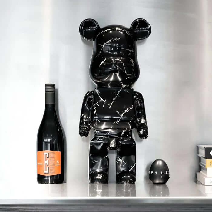 Black marble-effect resin bear sculpture on a shelf beside a wine bottle, egg timer and stacked books.