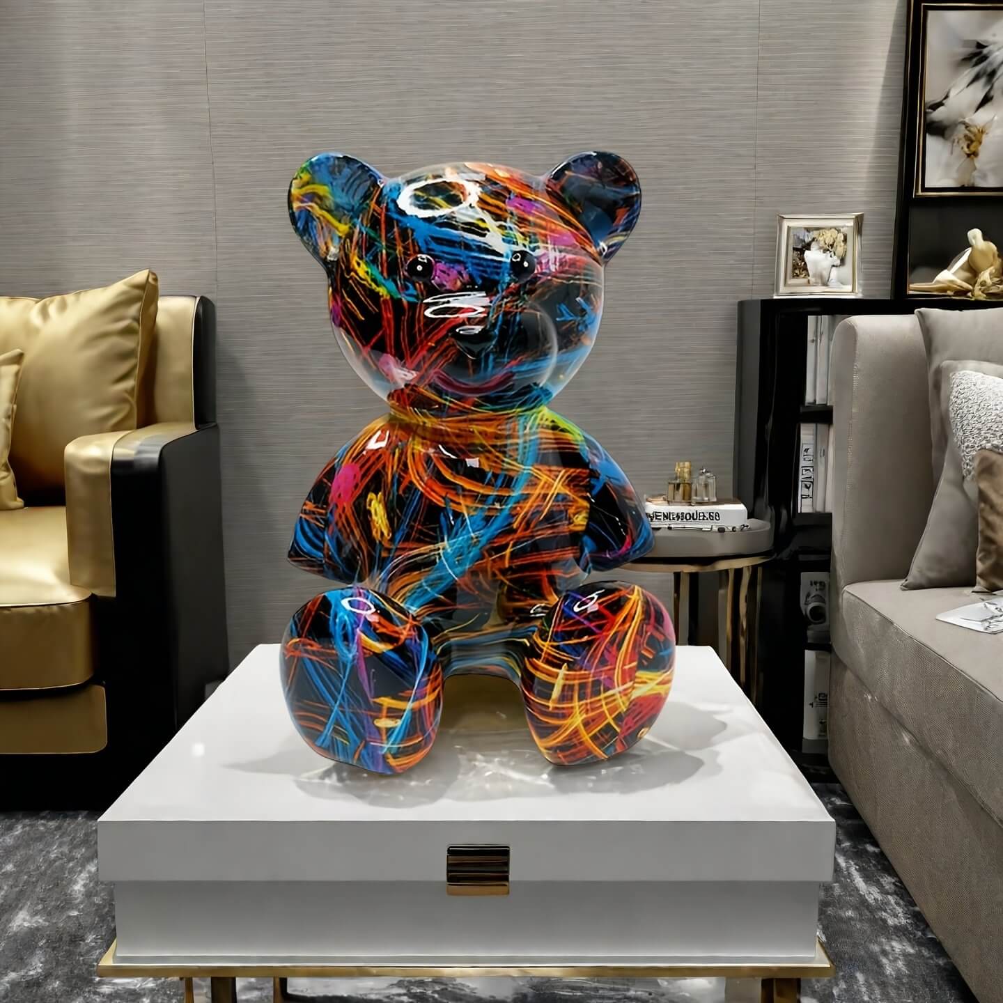 A glossy bear-shaped sculpture covered in vibrant, graffiti-like streaks of color sits on a white coffee table in a modern living room with gold and gray accents.