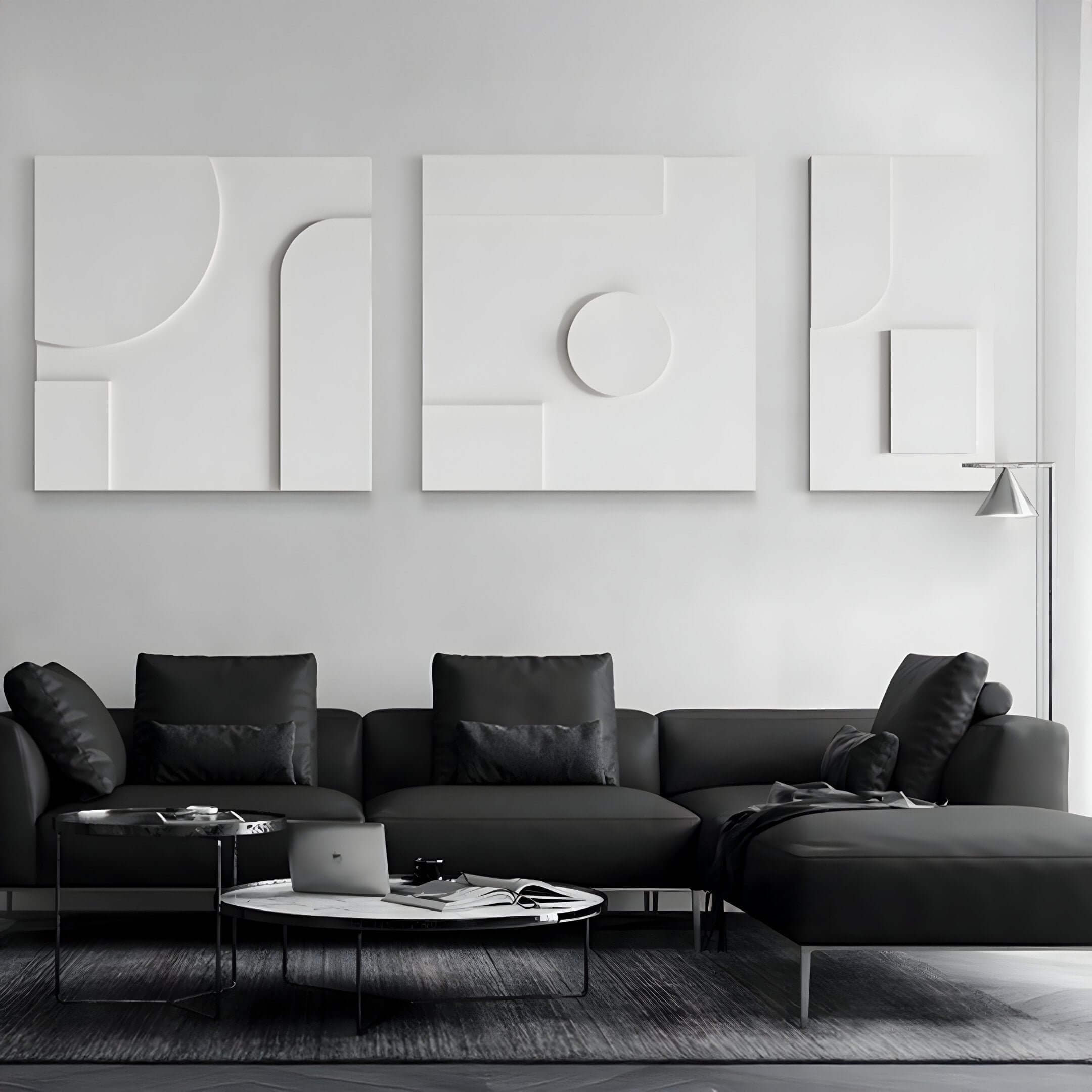 Minimalist triptych sandstone wall art in white relief, featuring abstract geometric shapes and clean 3D textures, displayed above a modern black sectional sofa in a monochrome living room.