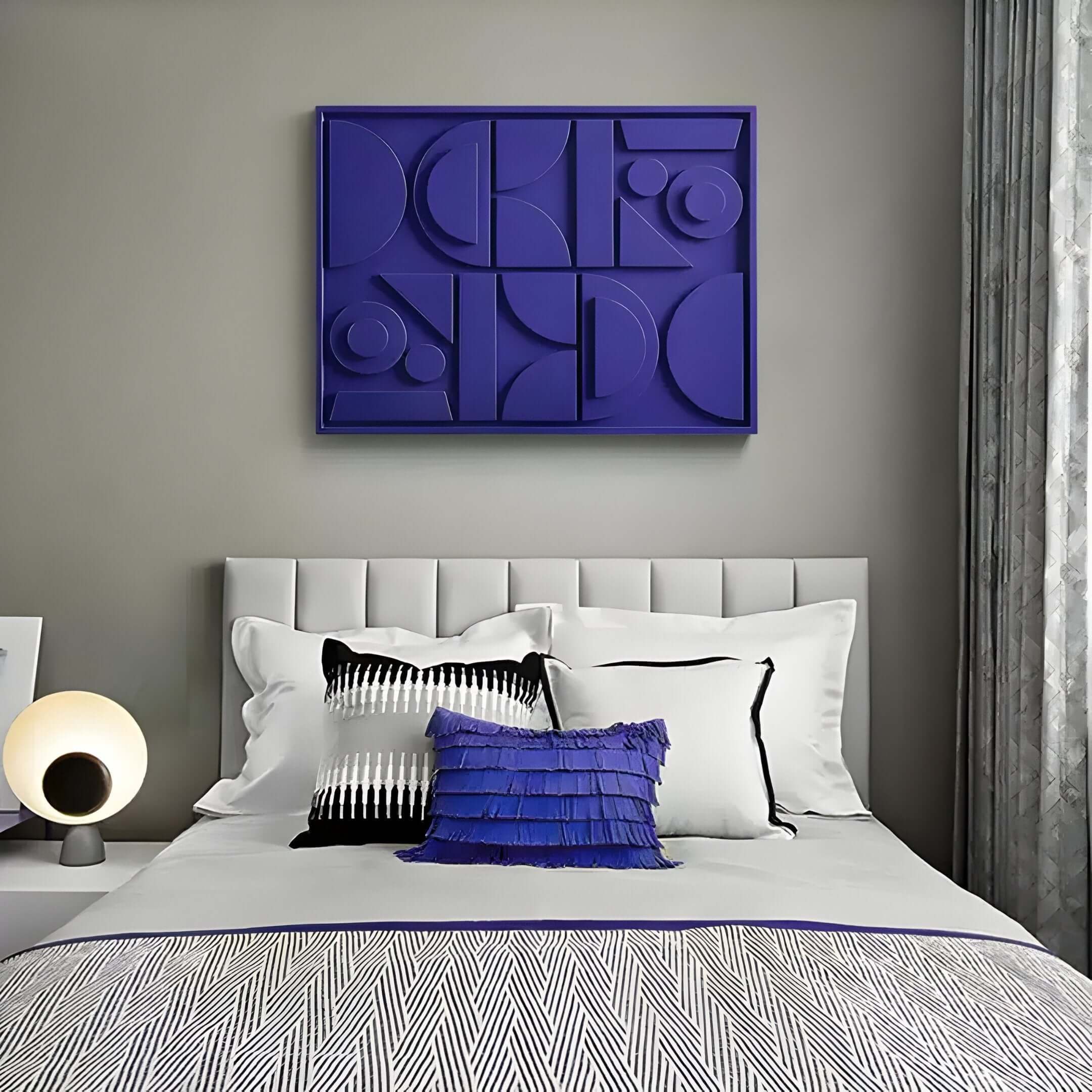 A modern bedroom features a white bed, geometric zigzag patterned throw, and blue accent pillows. A round lamp sits on the nightstand. Giant Sculptures Formate Royal Purple Geometric Wood Painted 3D Wall Art hangs on the gray wall, framed by grey and white curtains.