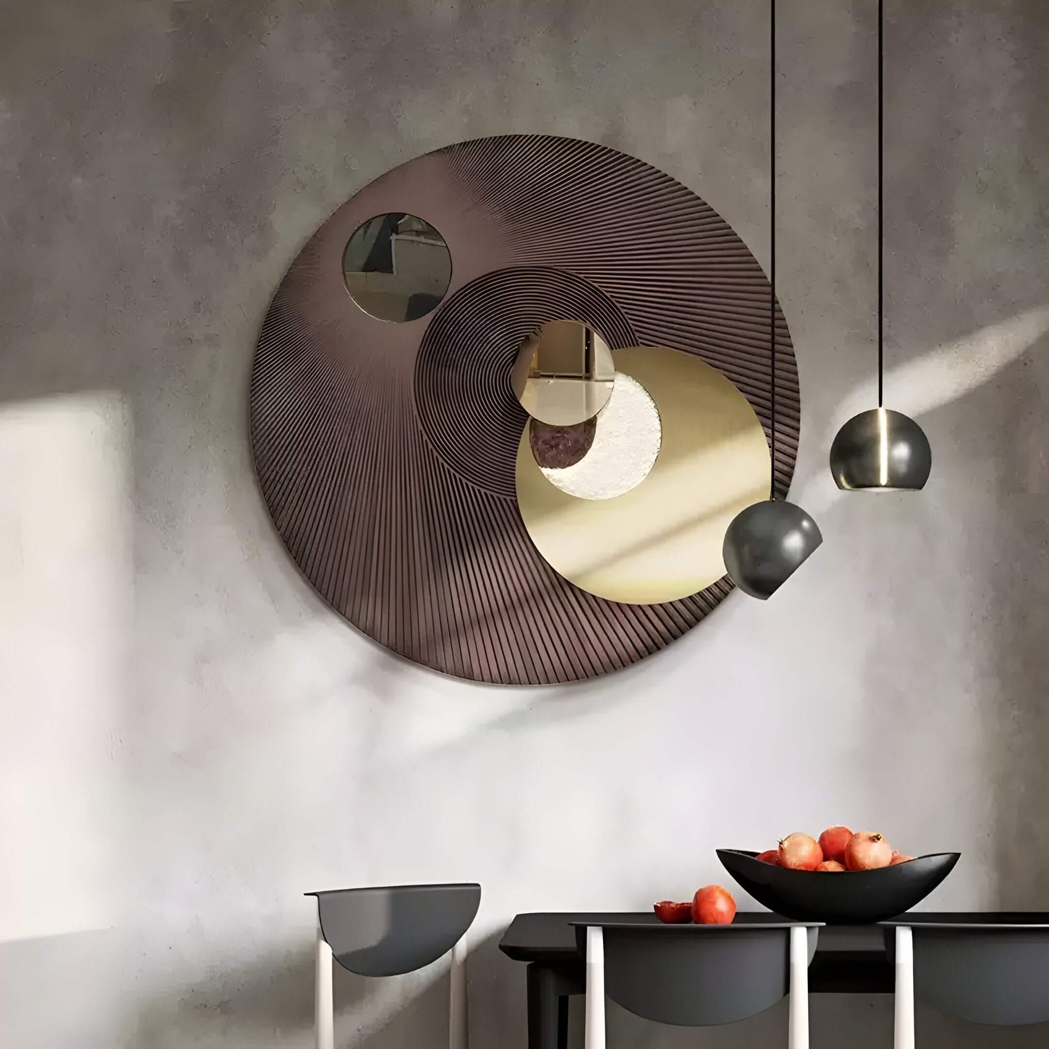 Modern round abstract wall mirror art above a black dining table with pendant lights and fruits.