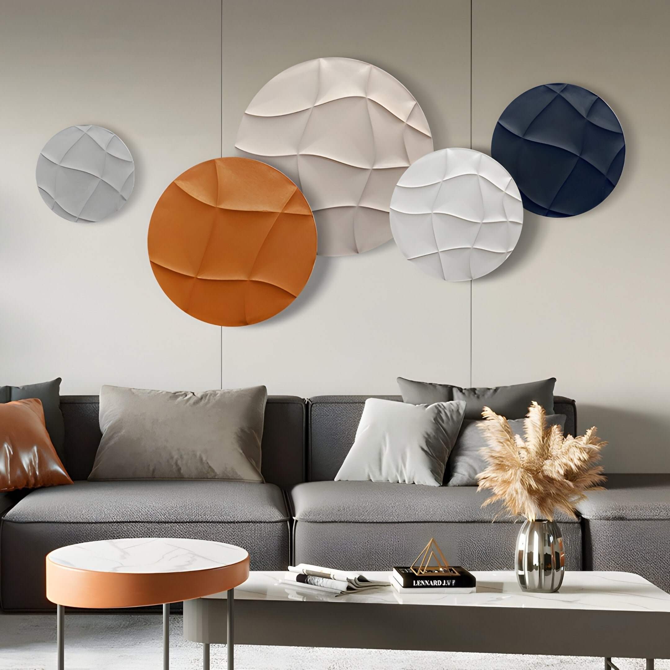 A modern living room boasts a gray sofa with assorted pillows, a small round table, and a vase of dried flowers. The wall displays Giant Sculptures Orbita 5-Set Circular Terra & Ivory Wall Art featuring 3D wood relief textures in white, orange, beige, and blue.