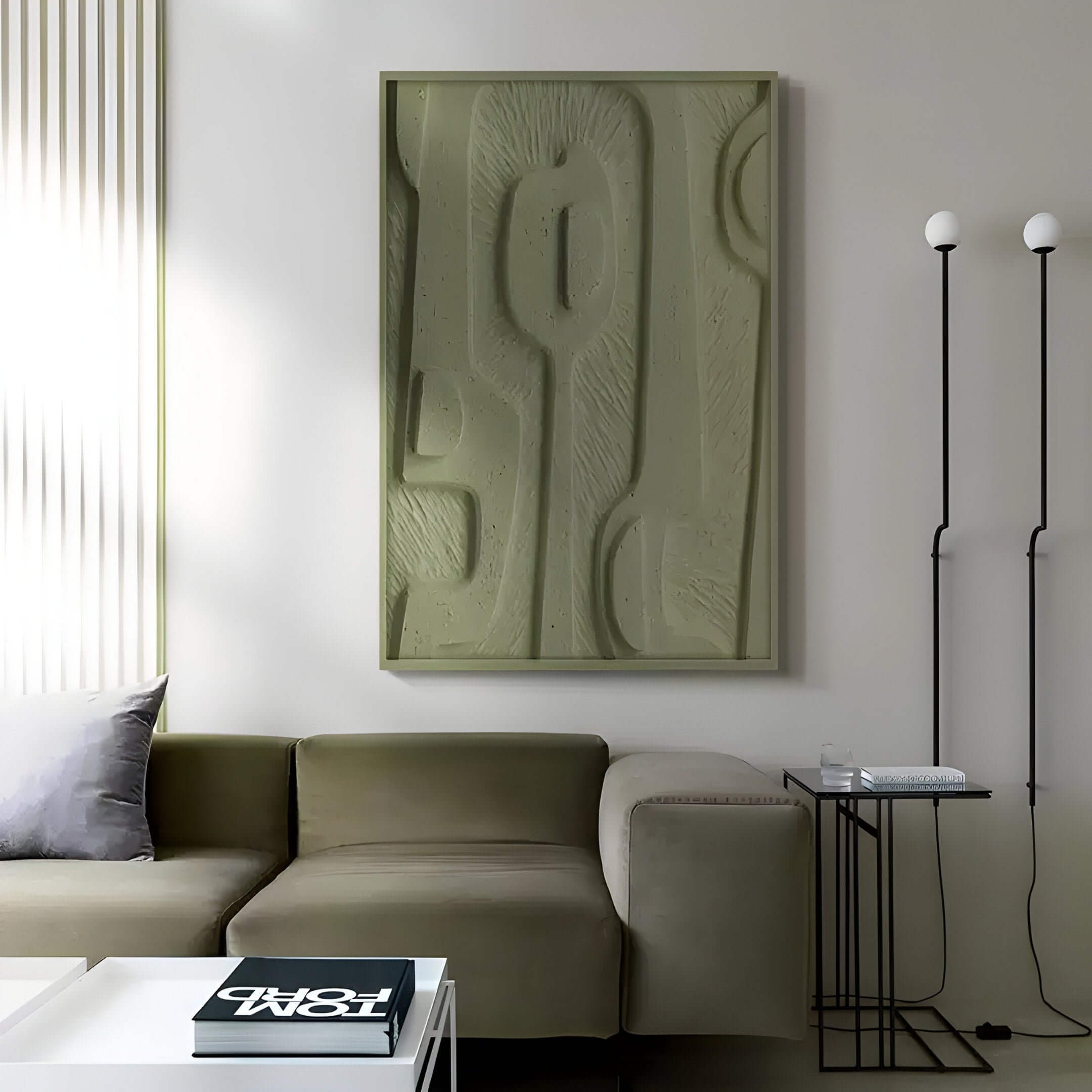 A modern living room features nature-inspired decor with the Terravura Rectangular Olive Green I 3D Wood Relief Wall Art by Giant Sculptures above an olive green sectional sofa. A white coffee table with a magazine sits nearby, complemented by a tall black floor lamp with two round bulbs.