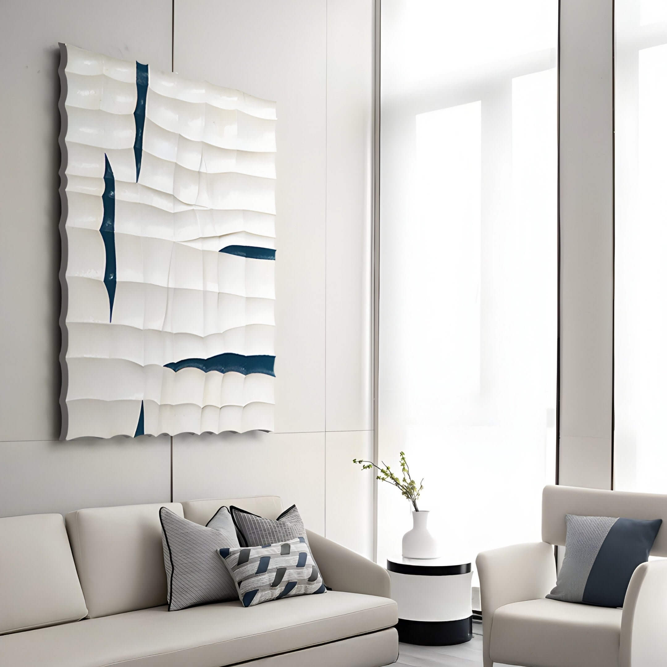 In a modern minimalist living room, a white sofa and armchair with gray cushions and blue accents set the scene. Above, the Striata White & Blue Wood Carving 3D Wall Art by Giant Sculptures adds dimension. A small round table with a white vase sits between the seating.