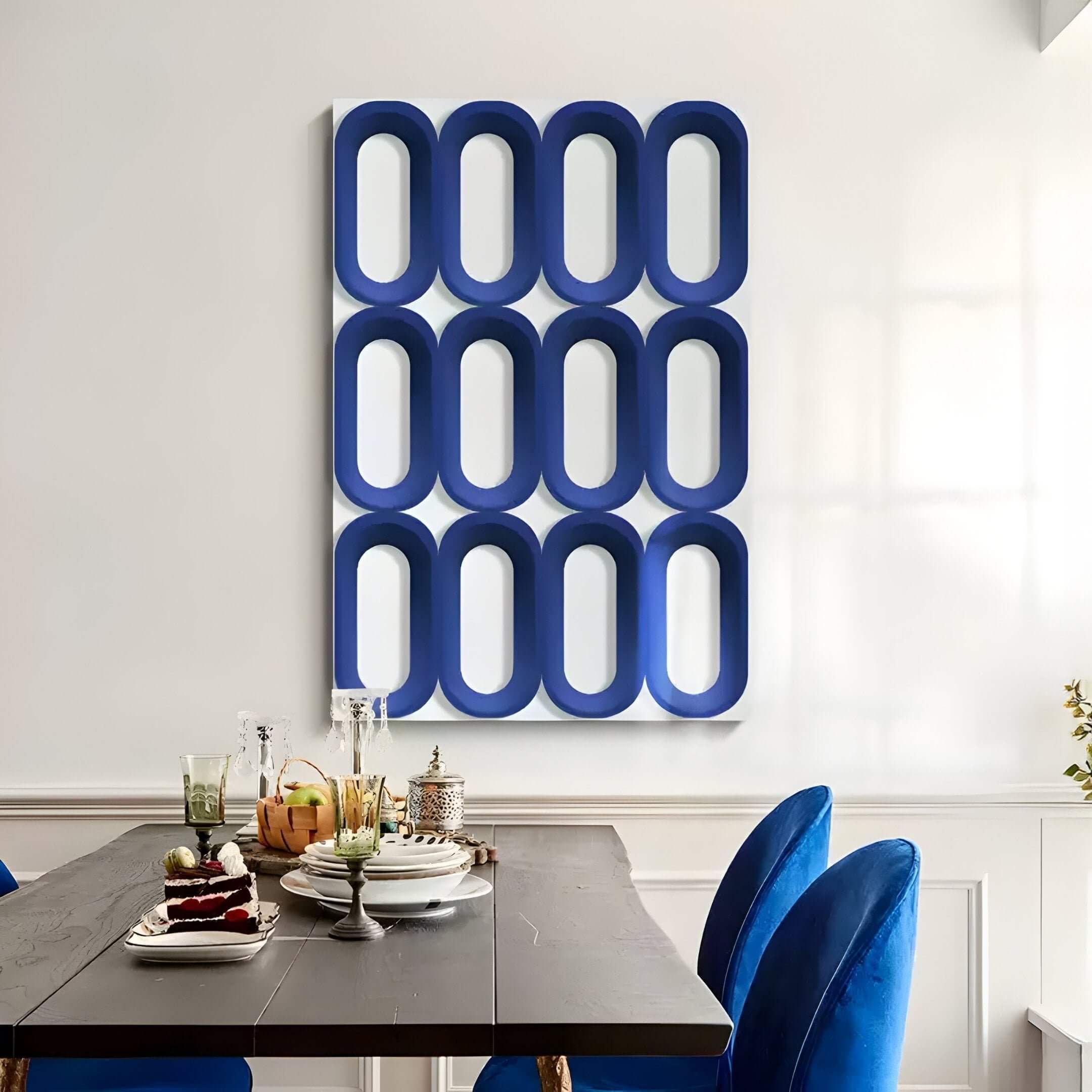 A modern dining room features a dark wood table set for dessert and drinks, with bright blue velvet chairs. On the wall, Revela White & Blue Geometric Wood Relief 3D Wall Art by Giant Sculptures adds striking 3D style with bold, oval forms.