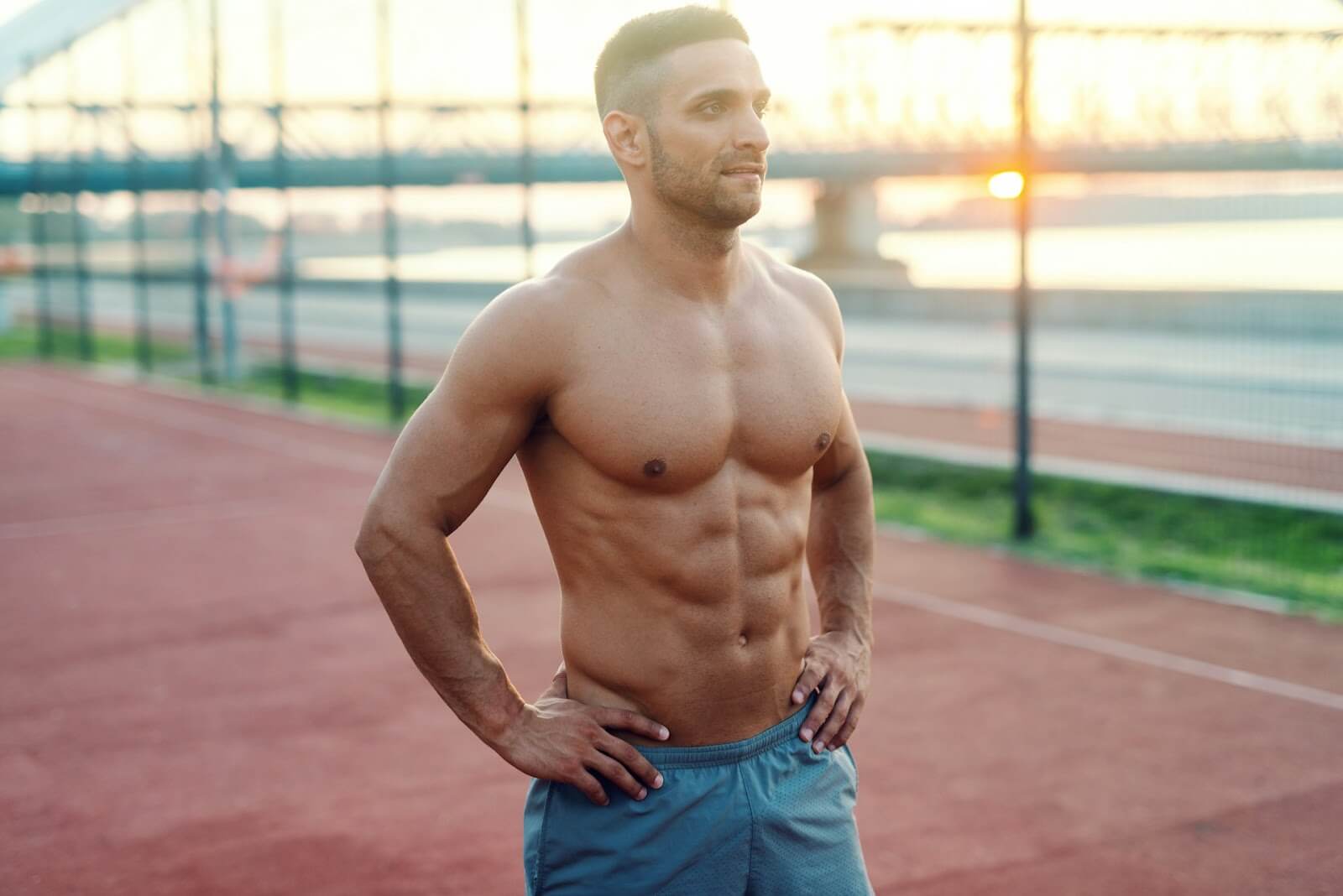 A shirtless man with a six pack standing confidently on a sports field