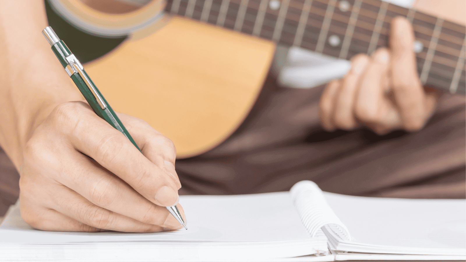 Person learning how to write catchy hooks in a notebook in a music studio, with a guitar.