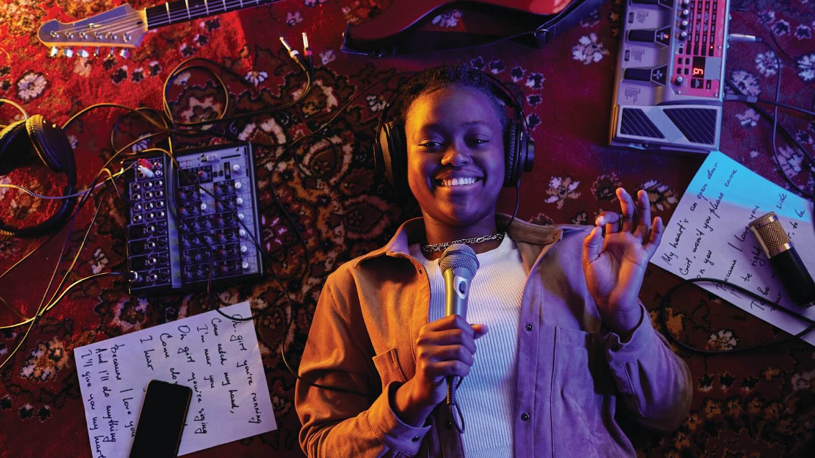 A musician lies on her carpet, surrounded by audio equipment and handwritten notes, as she learns how to write lyrics.