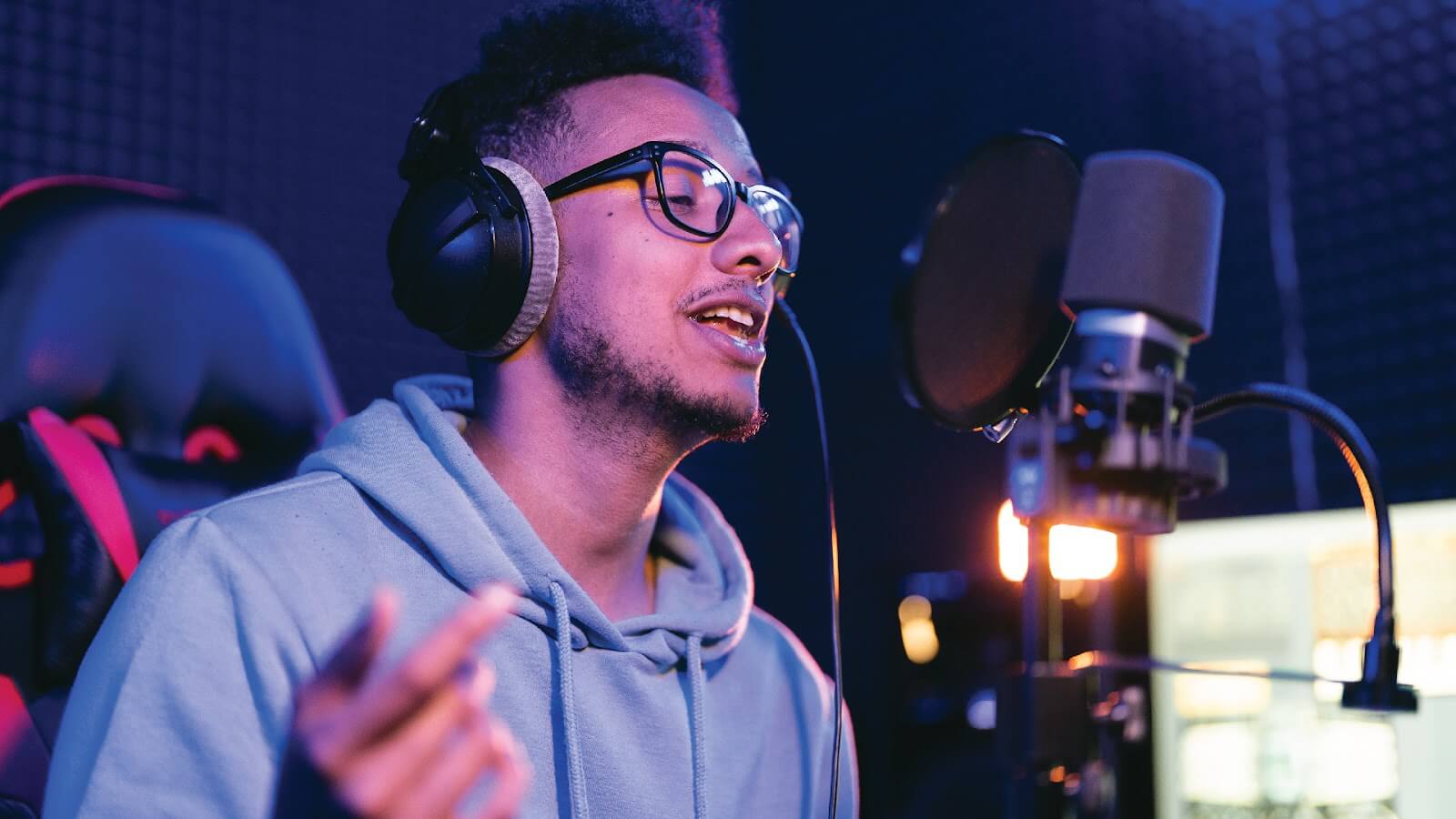 A man recording in a professional studio wearing headphones and a hoodie, learning how to make a rap song.