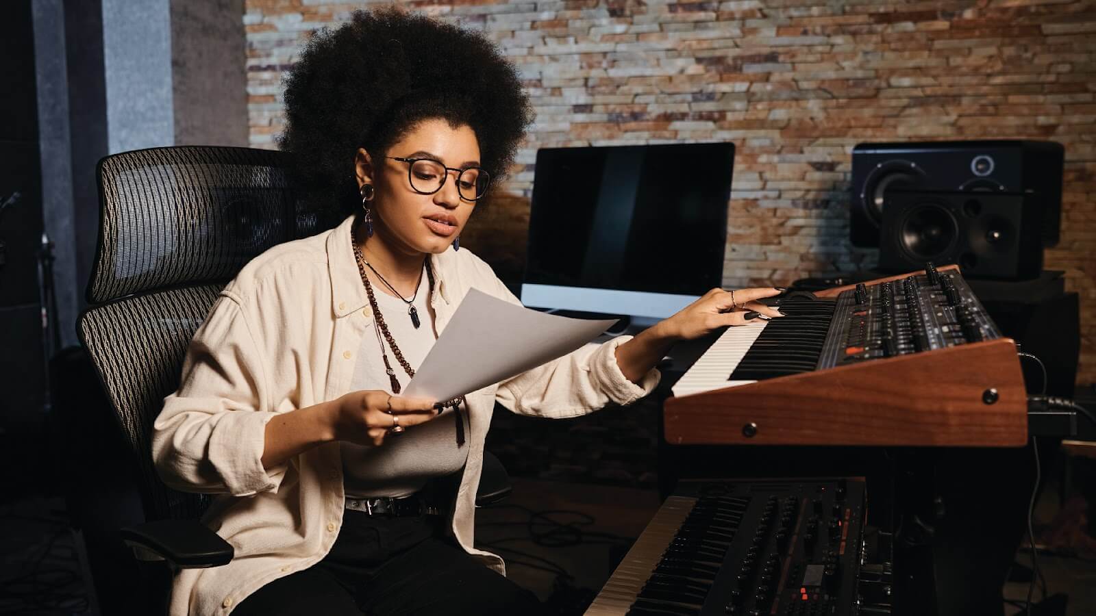 Musician in a studio holding a paper while playing a keyboard, showcasing the creative process of how to become a songwriter.