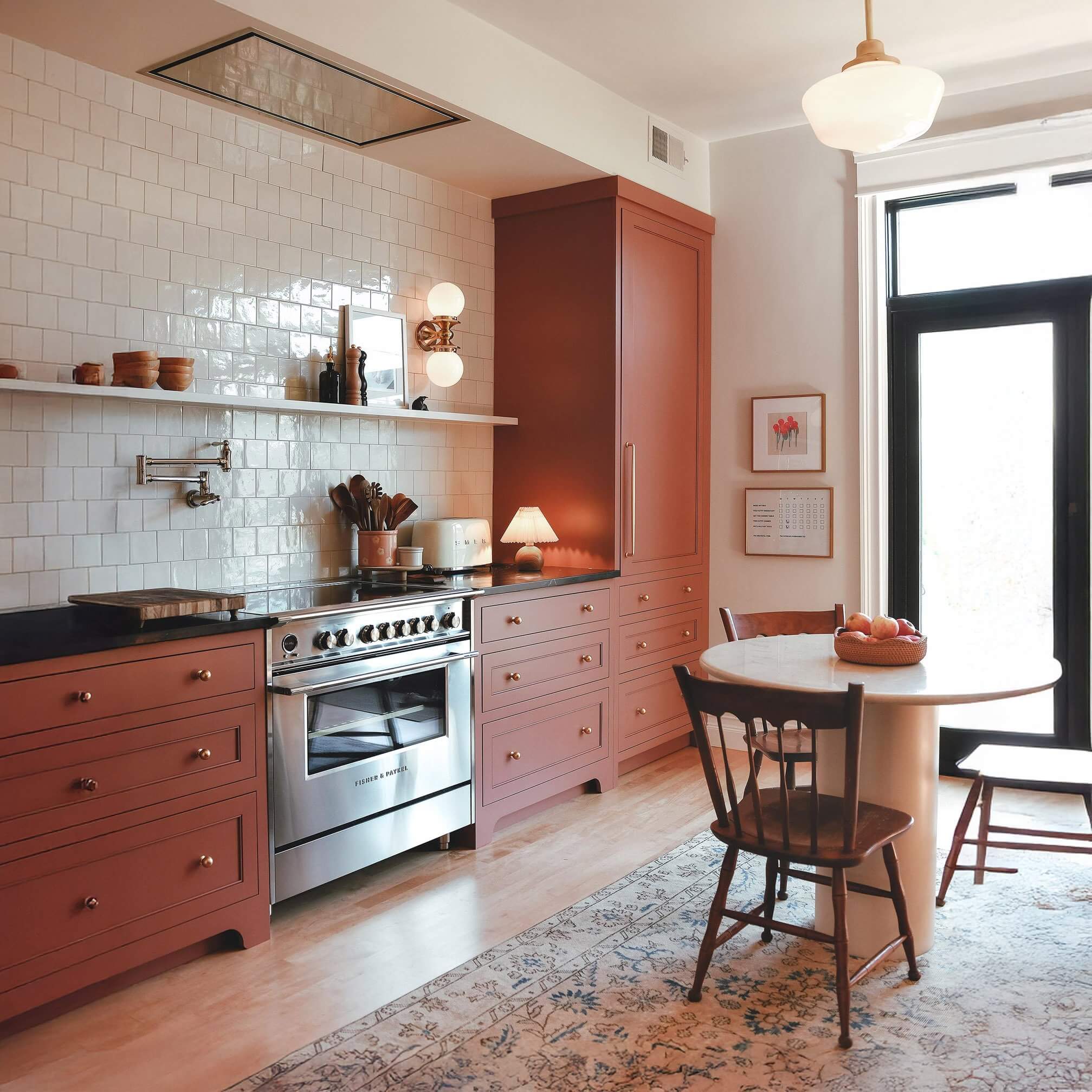 Warm-toned kitchen with blush cabinetry, vintage rug, and natural light by a round table and wooden chairs.