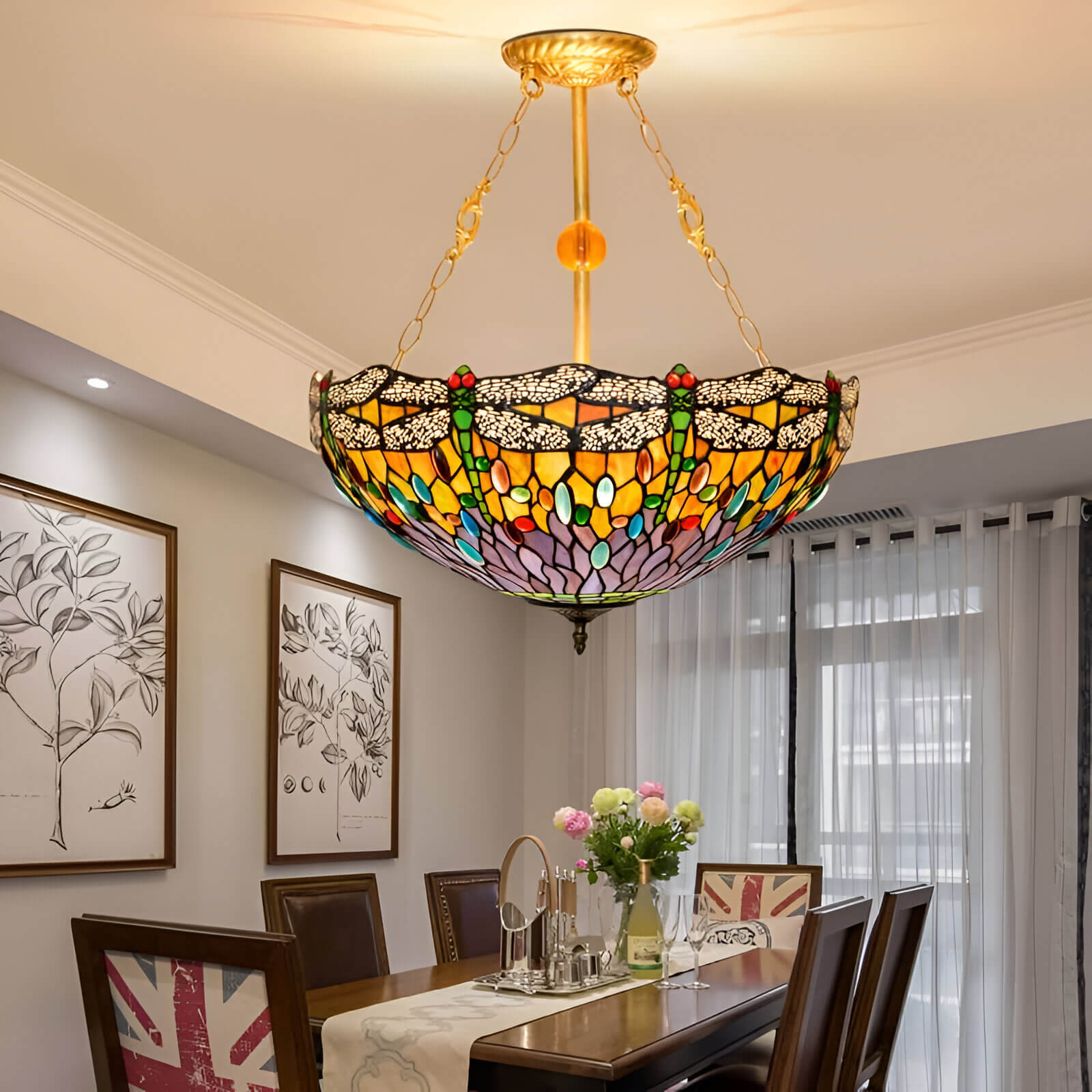 Multicolored Tiffany-style bowl pendant with chain suspension over a dining table in a bright, framed art-filled room