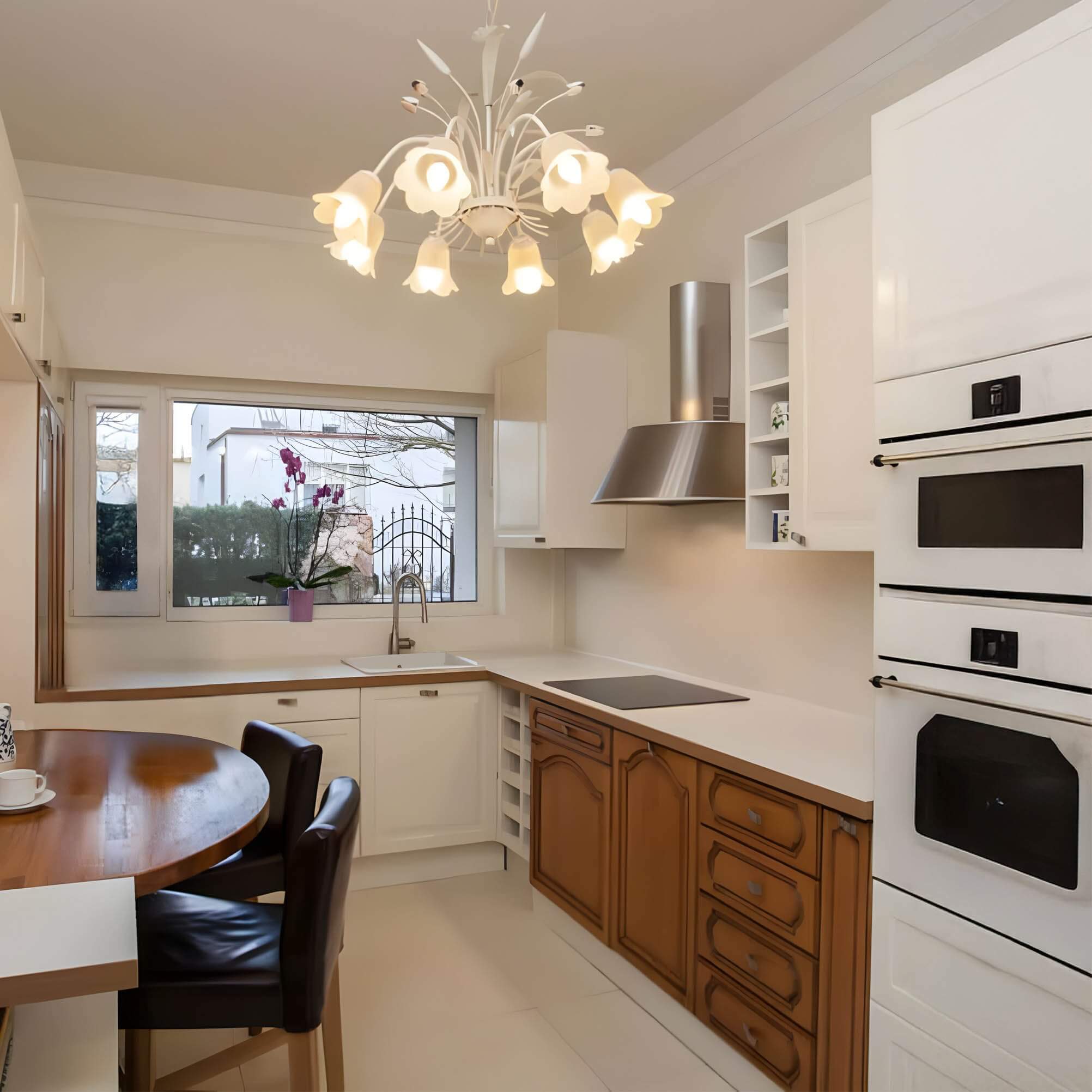 U-shaped kitchen with mixed white and wood cabinetry, floral chandelier, and breakfast nook.