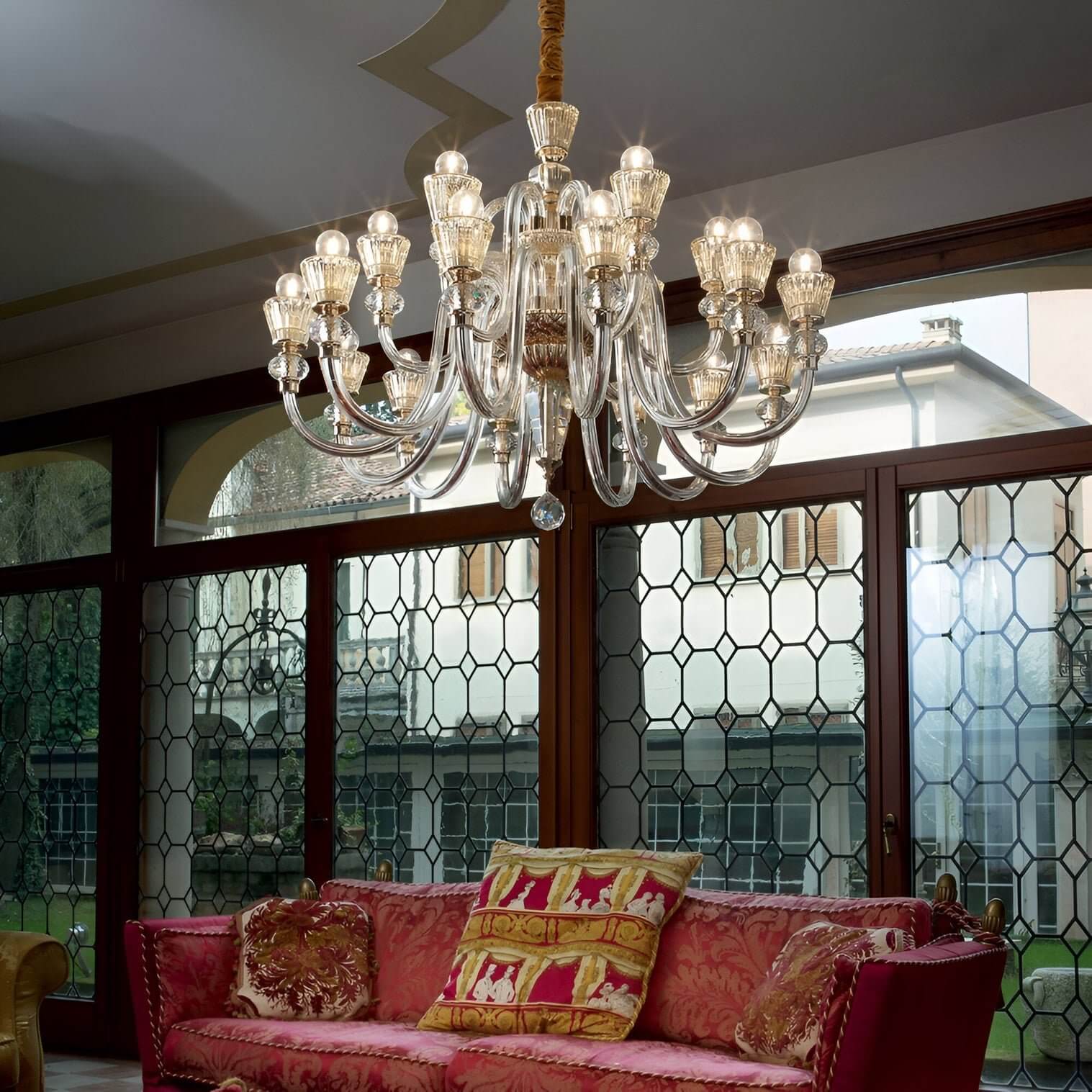 Luxurious glass chandelier with multiple branches and gold accents over a red sofa.