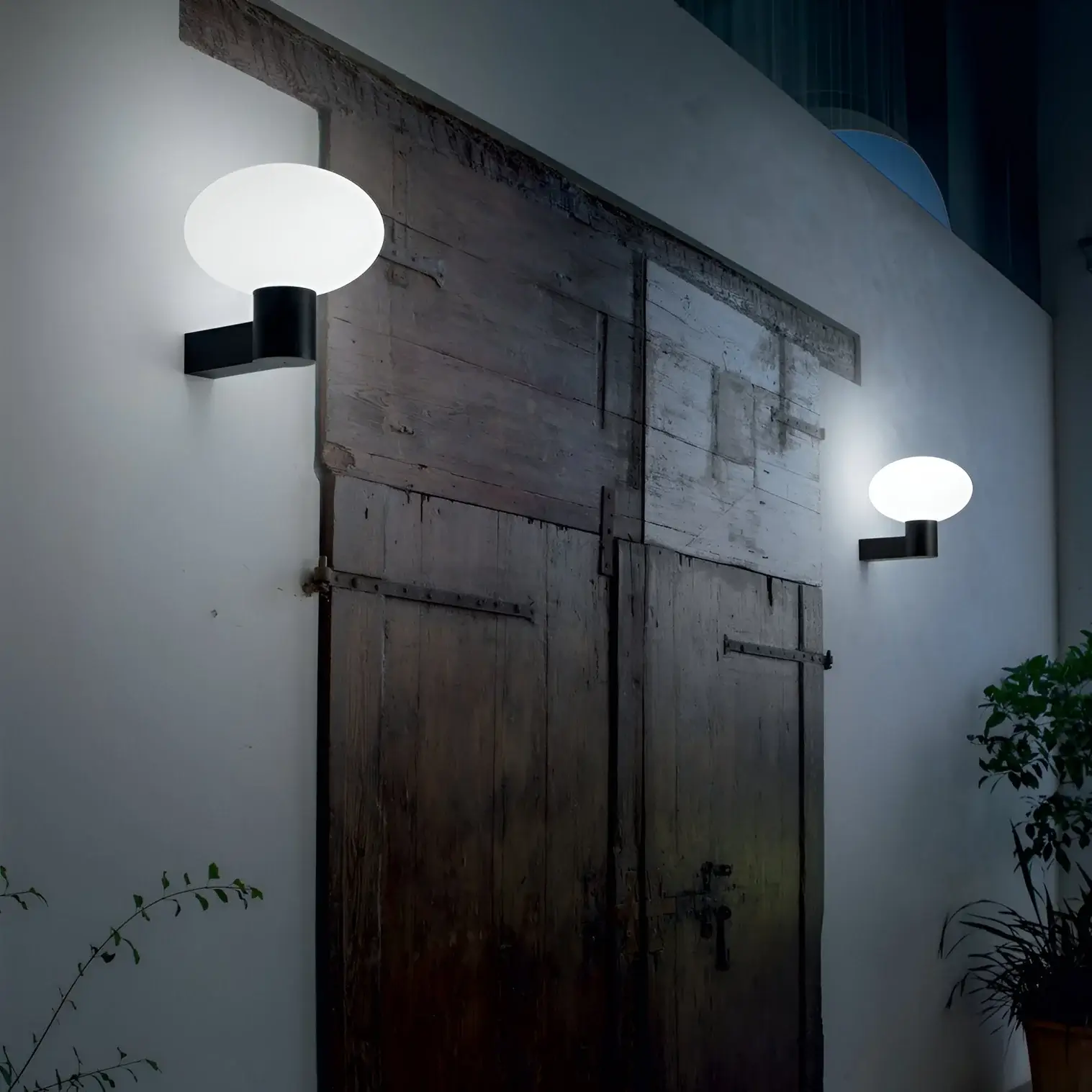Rustic wooden doors illuminated by round modern wall sconces with frosted glass, set against a white wall at night.