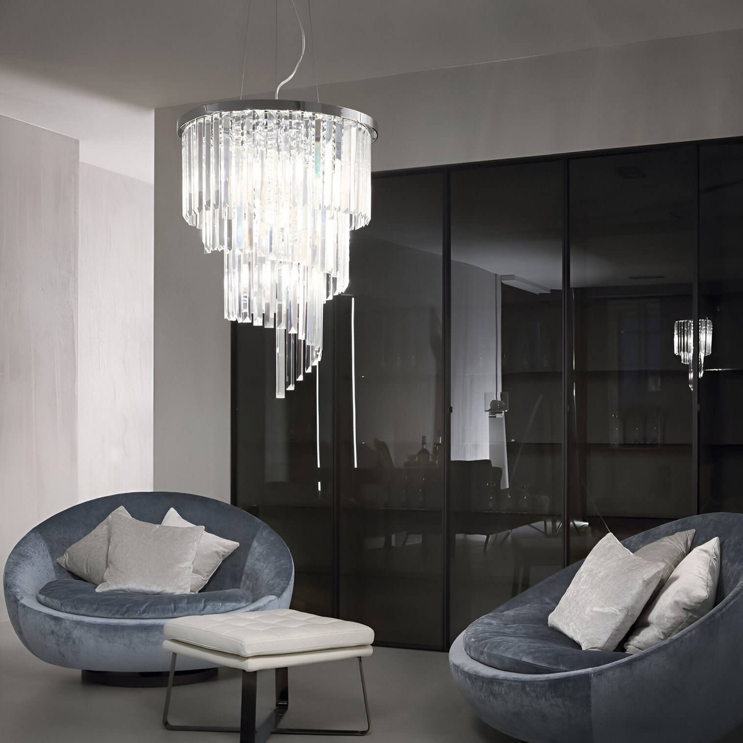 Tiered crystal chandelier with vertical prisms in a chrome frame hangs above a modern seating area with curved velvet chairs.